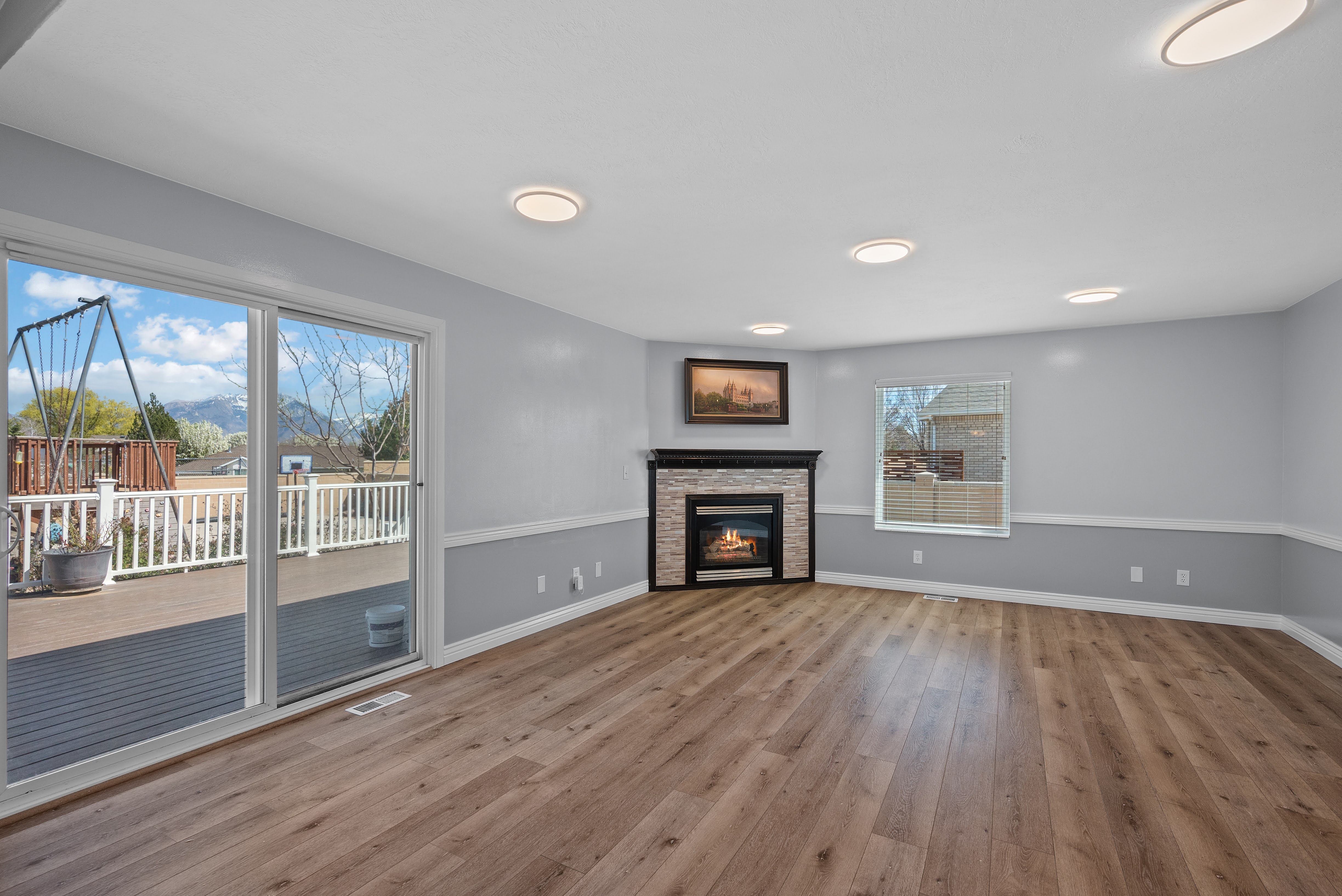 Spacious living area featuring wood-finish flooring, a contemporary fireplace with stone surround, and abundant natural light from a large sliding glass door