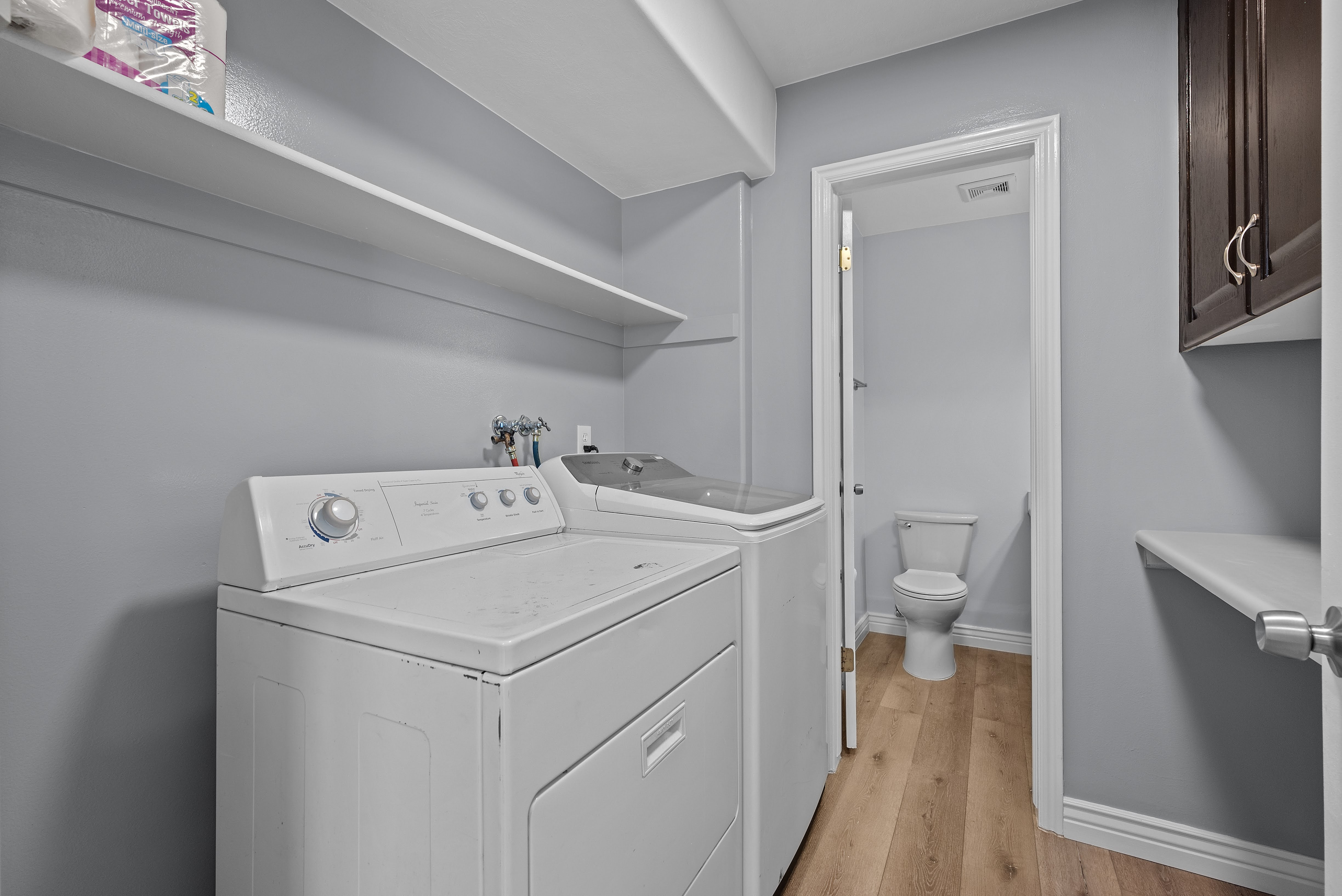 Laundry area with light gray walls, wood-finish flooring, and white wall shelving