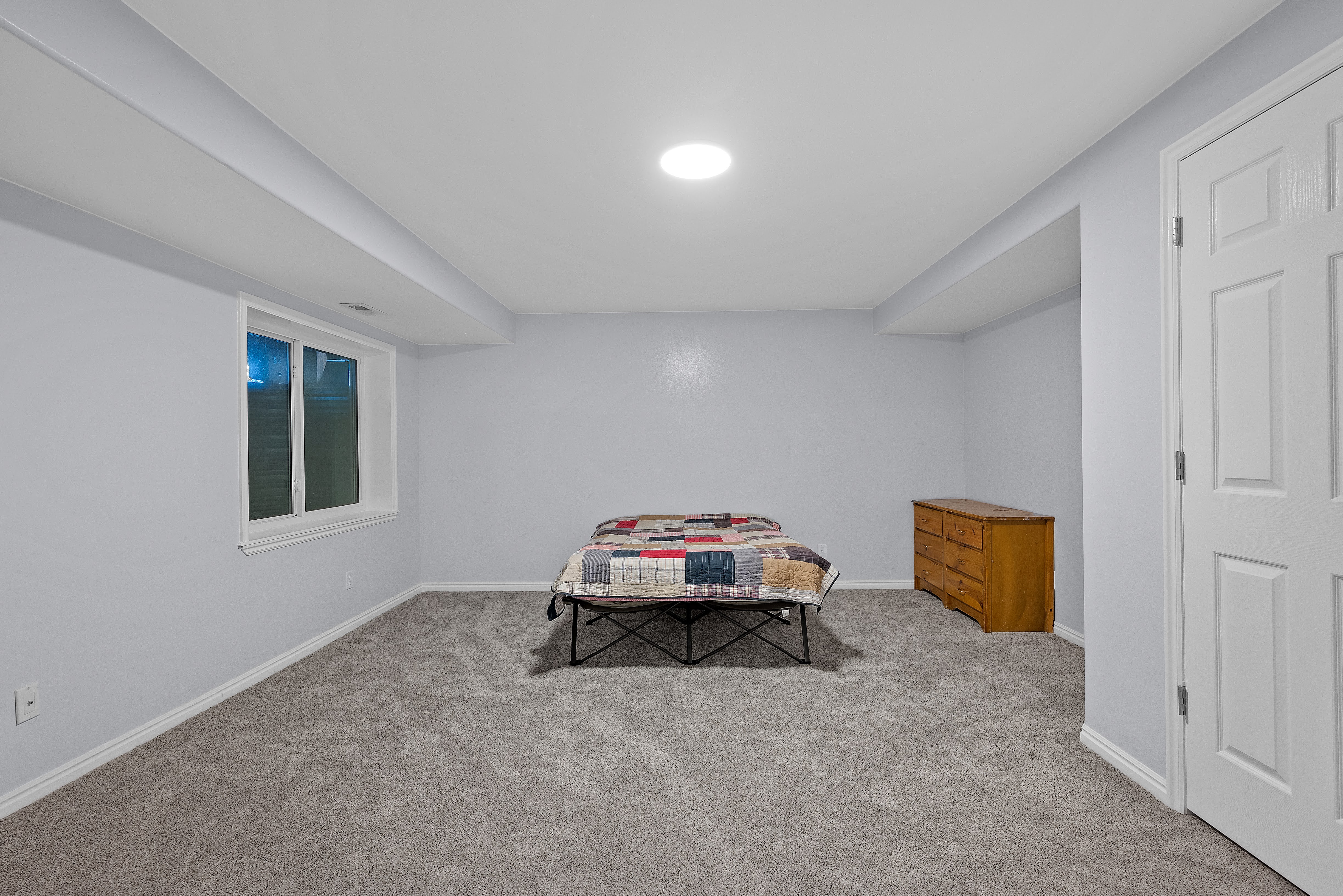 Spacious room featuring light gray walls, plush gray carpeting, white baseboards, and a white ceiling