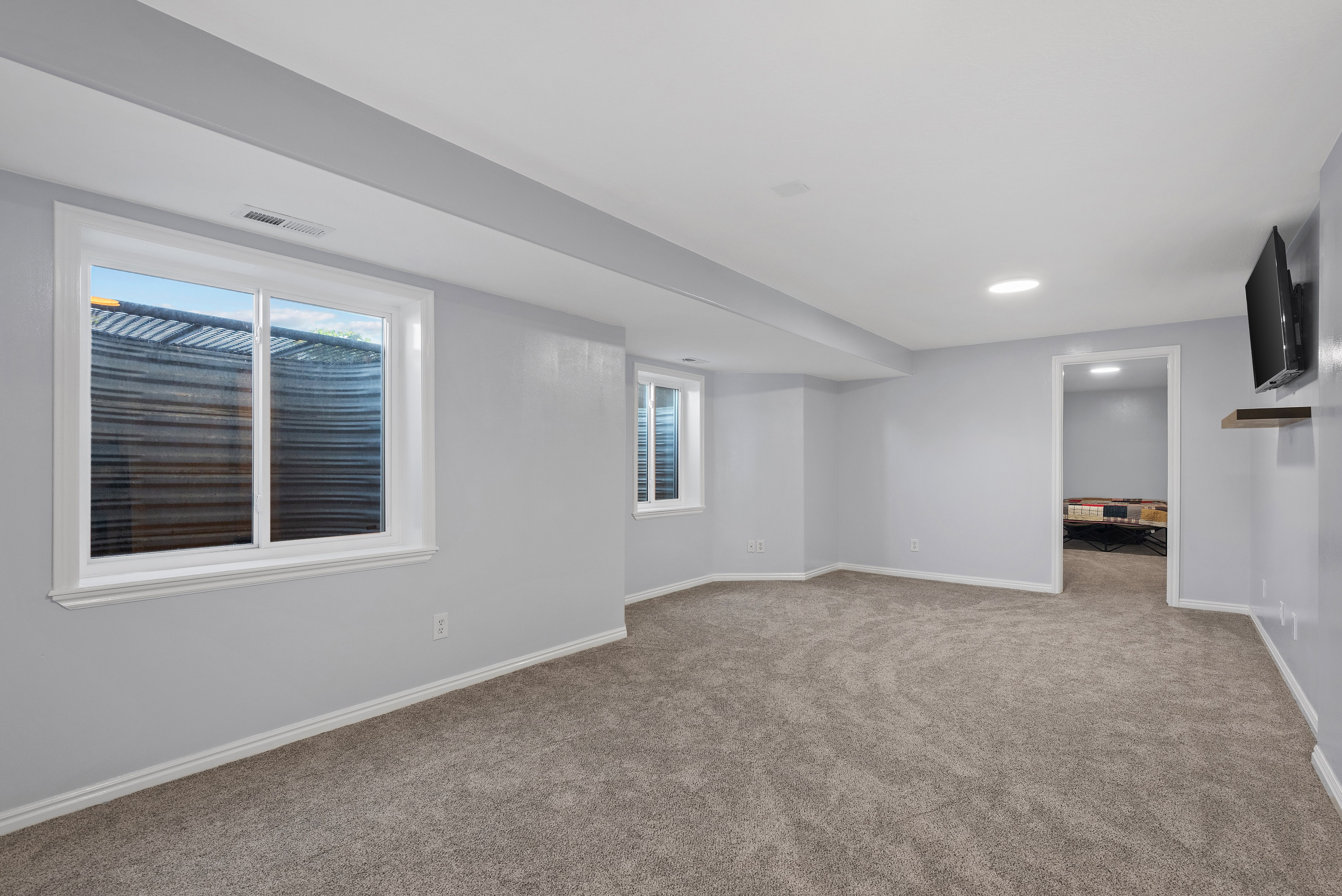 Carpeted room featuring multiple egress windows, light gray wall paint, white trim, recessed lighting, and a wall-mounted media shelf