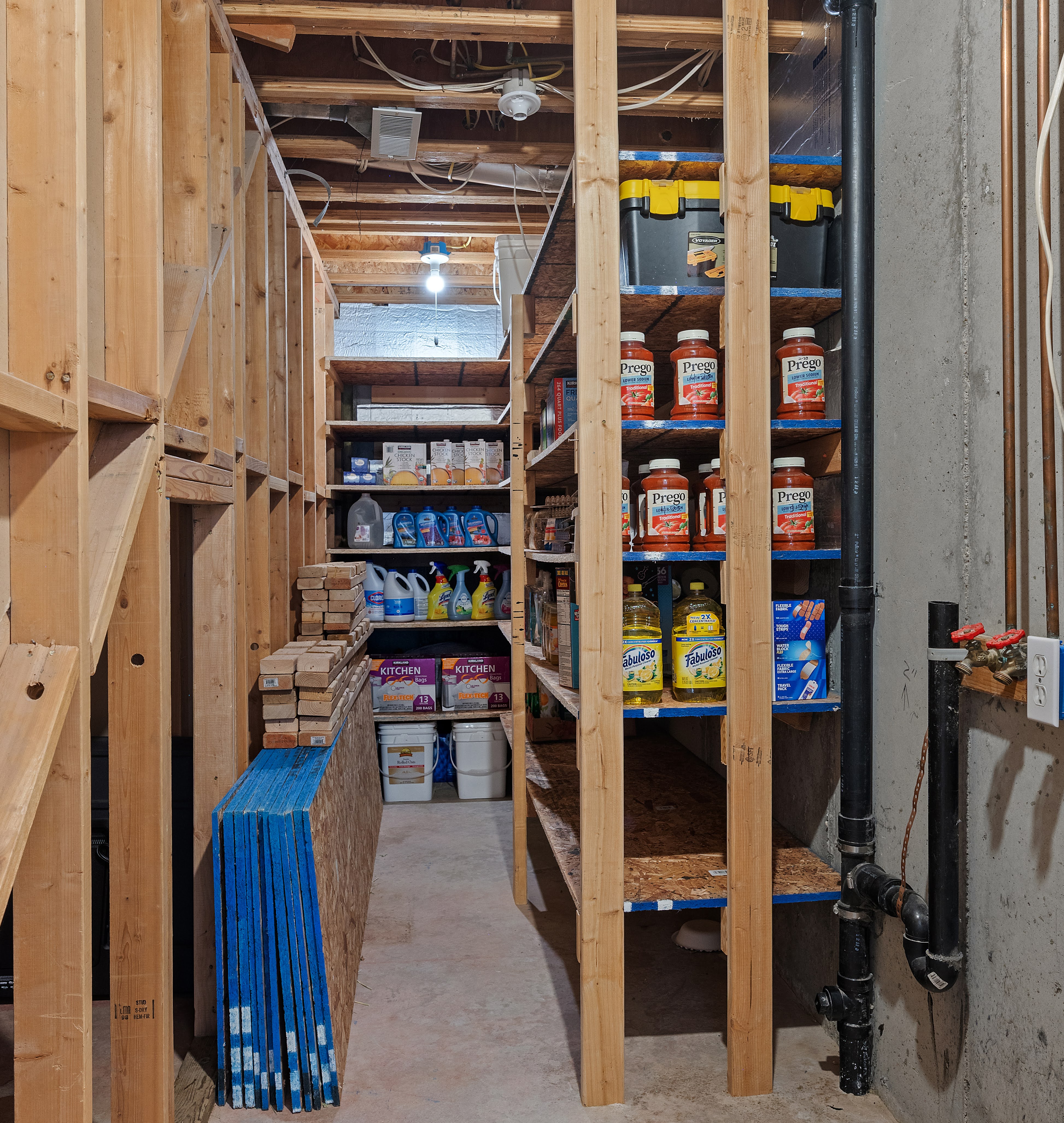 Unfinished basement area featuring exposed wood framing, concrete flooring, and built-in wood shelving for storage