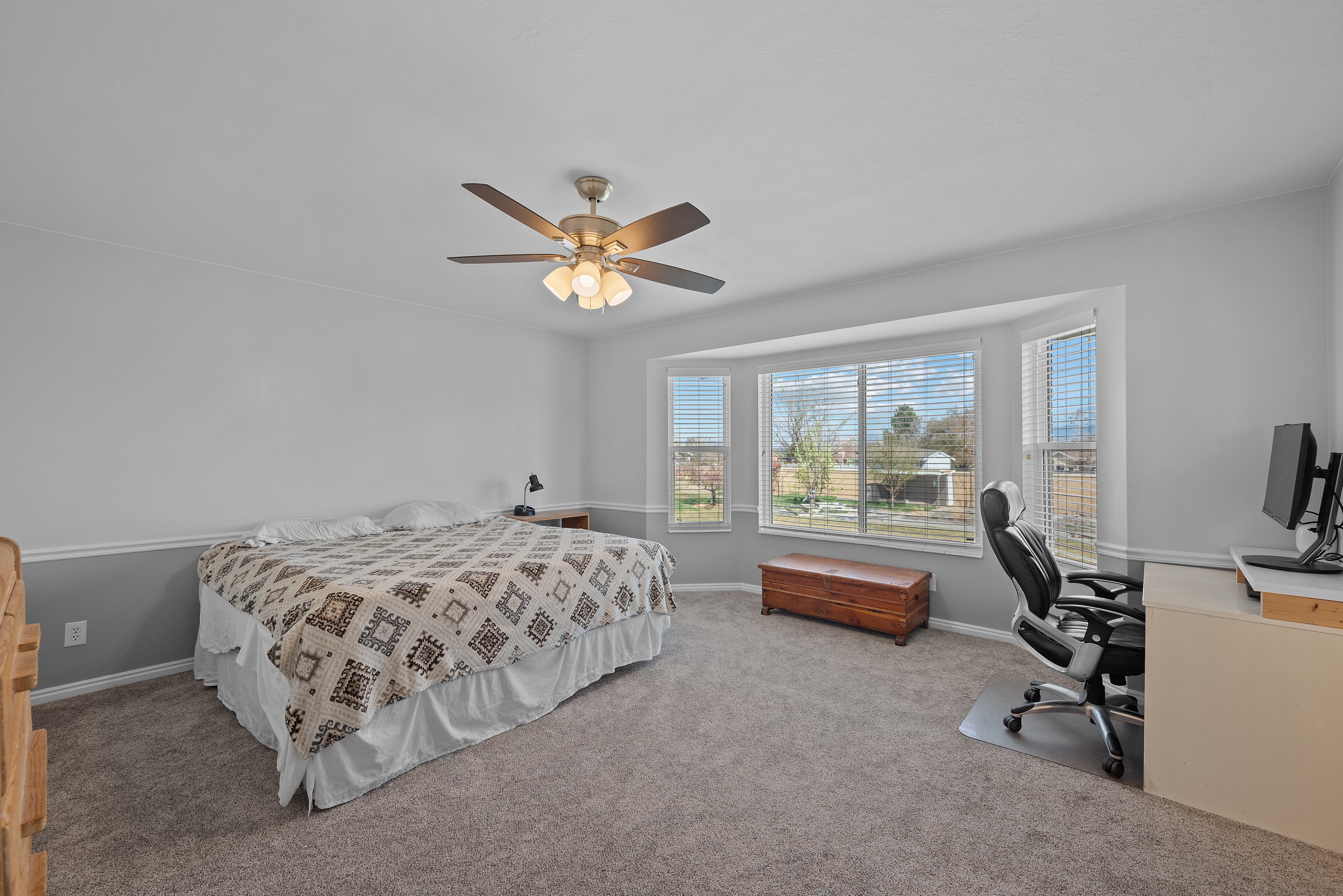 Carpeted bedroom featuring a bay window, ceiling fan with light fixture, and two-tone wall treatment