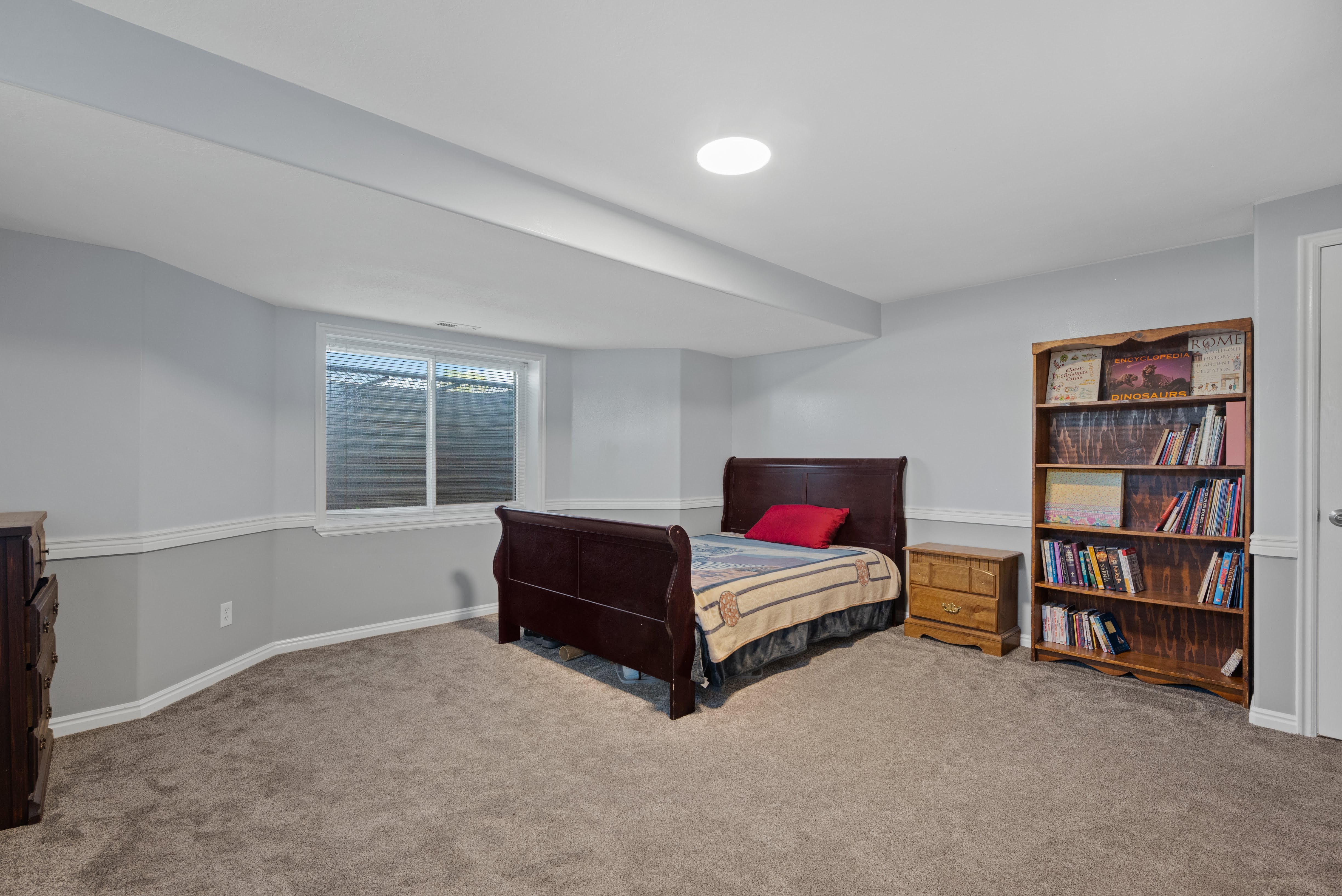 Spacious room featuring light gray walls with white chair rail molding, plush carpet flooring, a large egress window, and recessed ceiling lighting