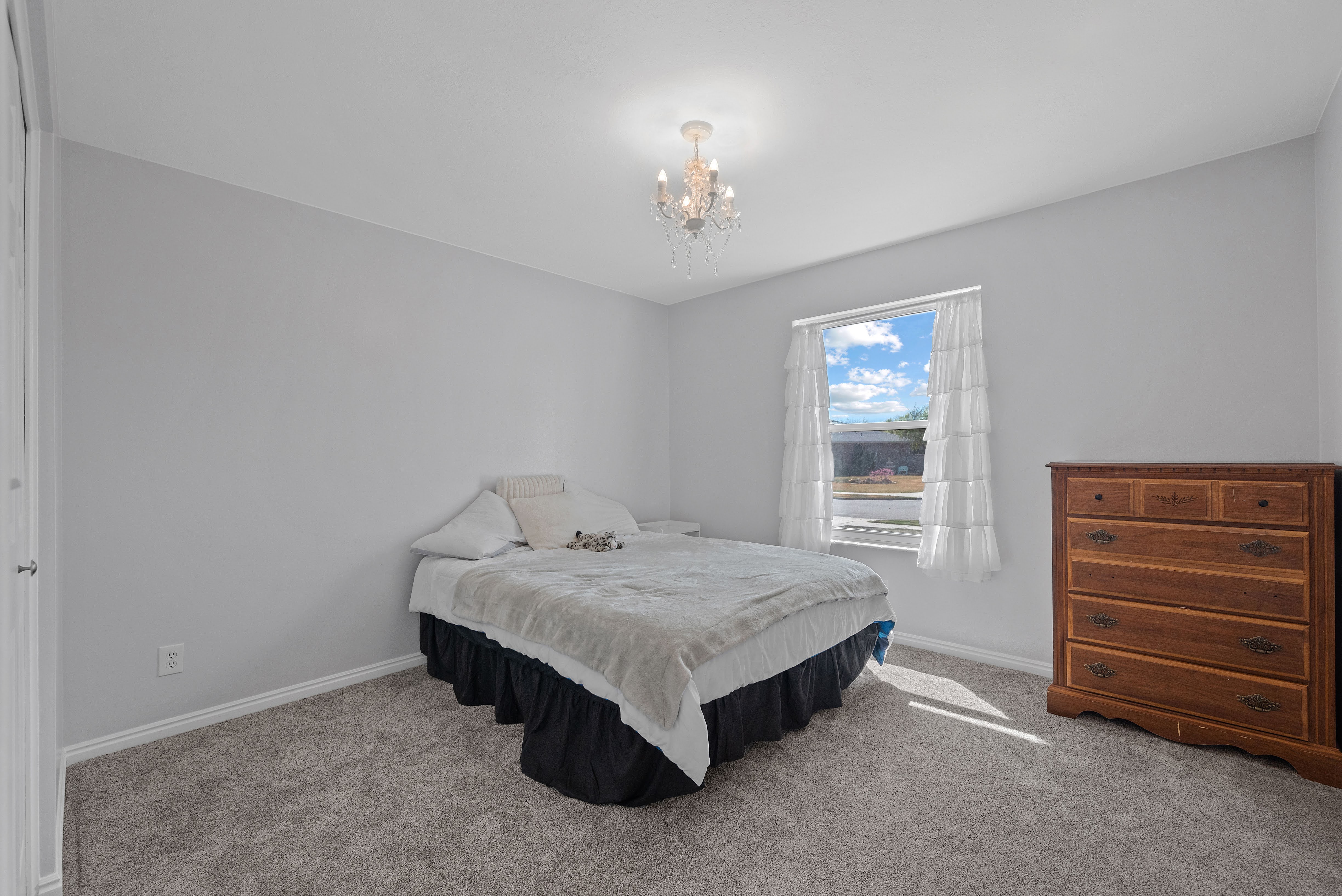 Bright interior with neutral gray walls, gray carpet, white trim, and a window featuring white sheer curtains