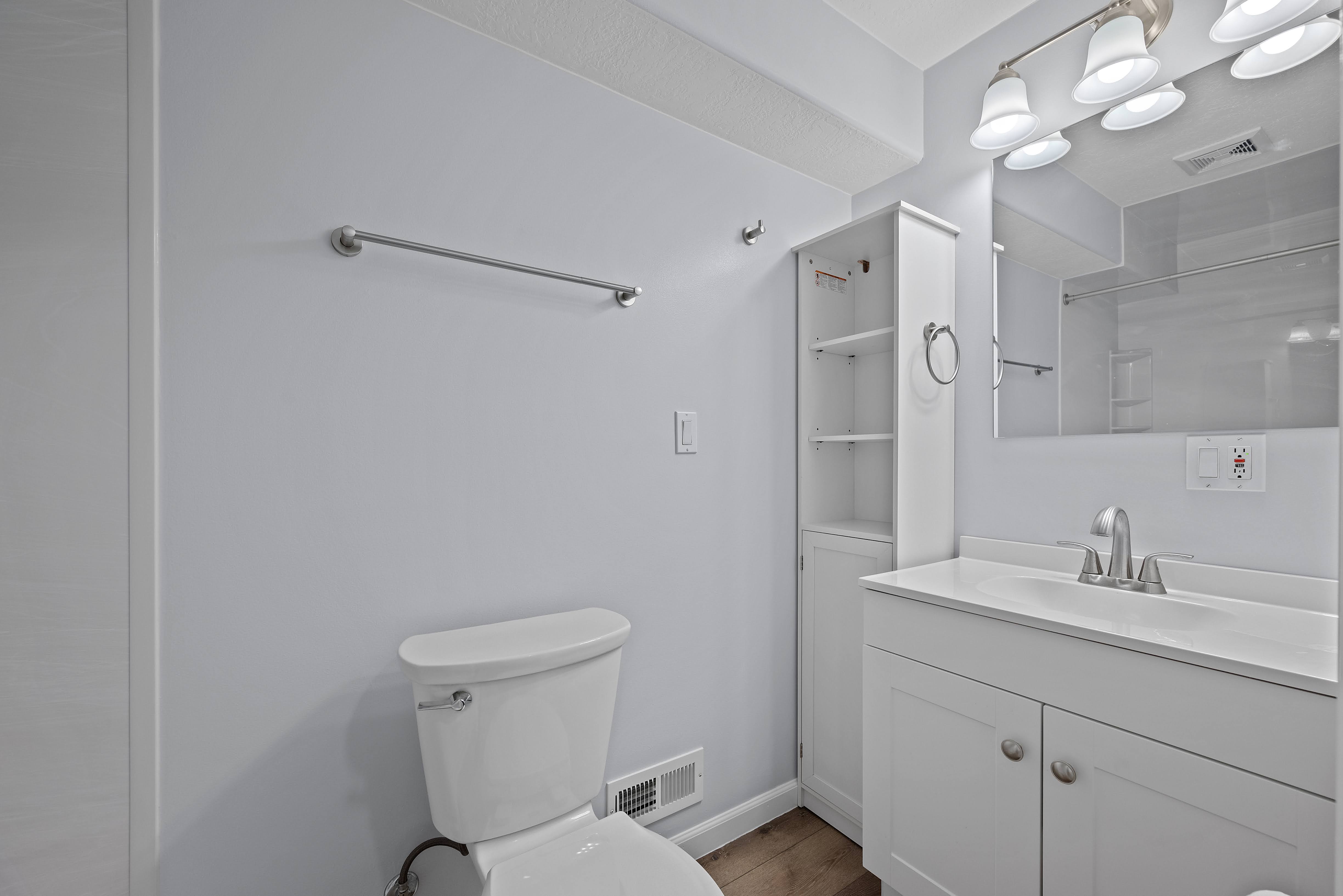 Bathroom featuring a white vanity with integrated sink, brushed nickel faucet, wall-mounted mirror, and overhead vanity lighting