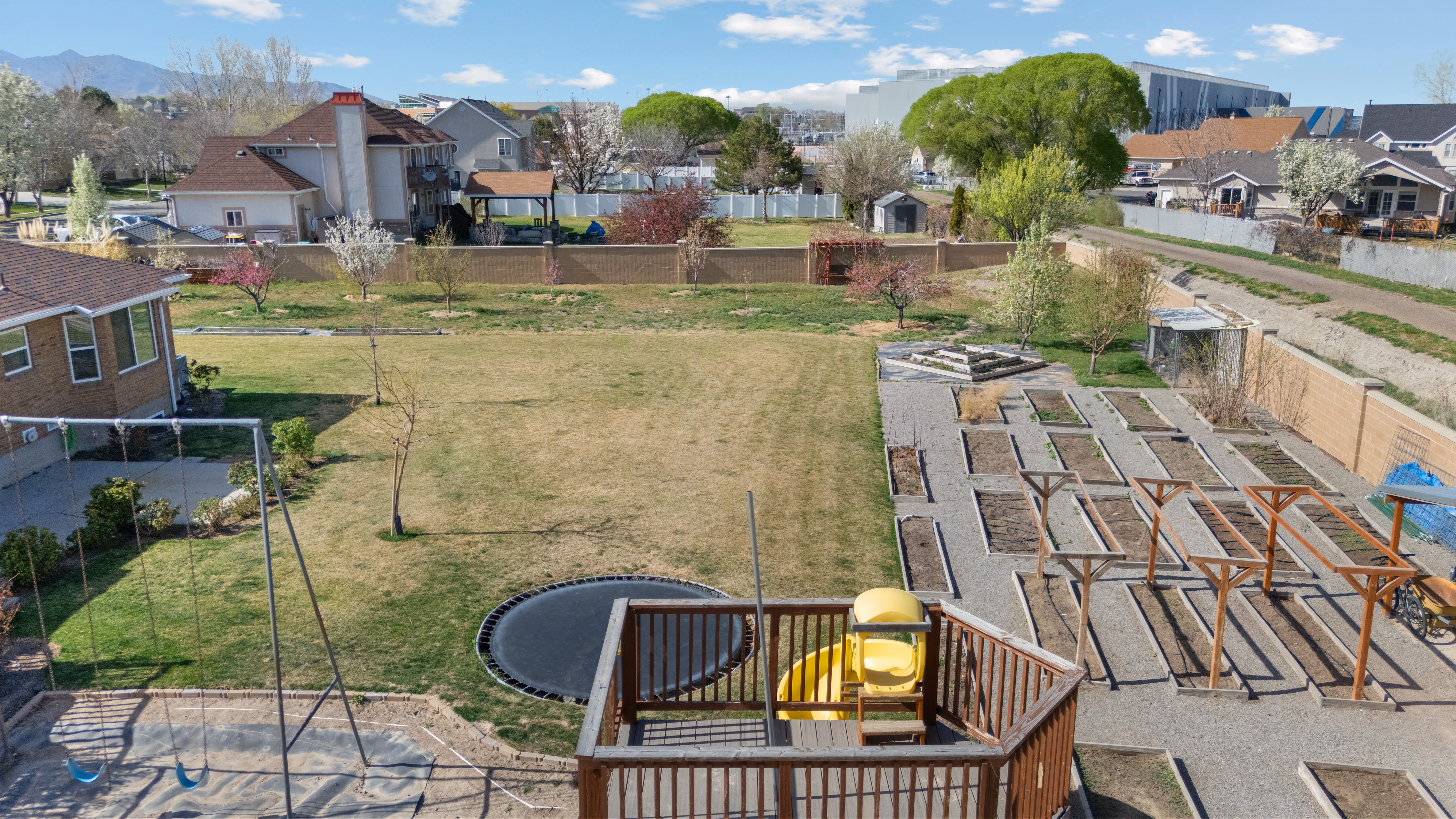 Expansive backyard featuring a large lawn, a dedicated garden area with multiple raised beds, and a multi-level wooden deck with railings