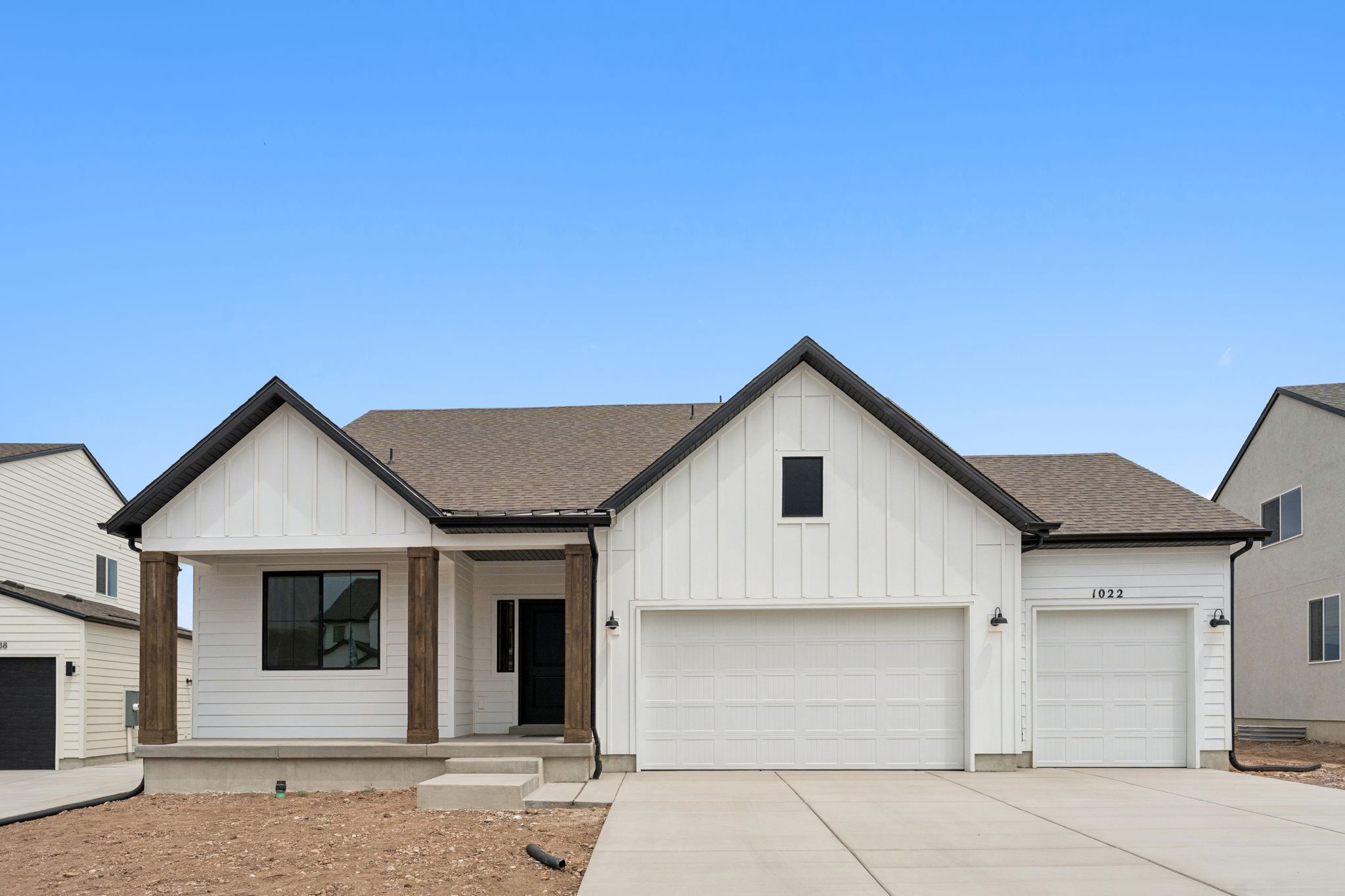 Modern farmhouse exterior featuring white board and batten siding, dark trim accents, and a covered porch with wood wrapped columns