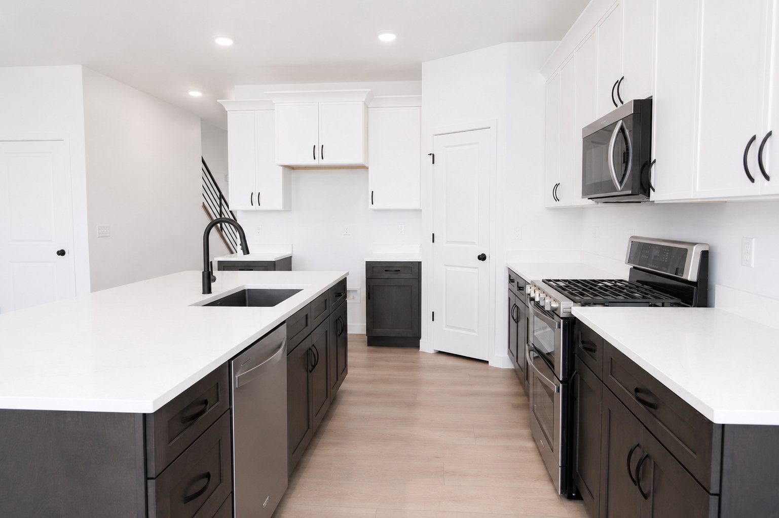 Modern kitchen featuring a large island with an undermount sink and matte black faucet, stainless steel appliances, white upper cabinetry, dark wood-finish base cabinetry, and recessed lighting