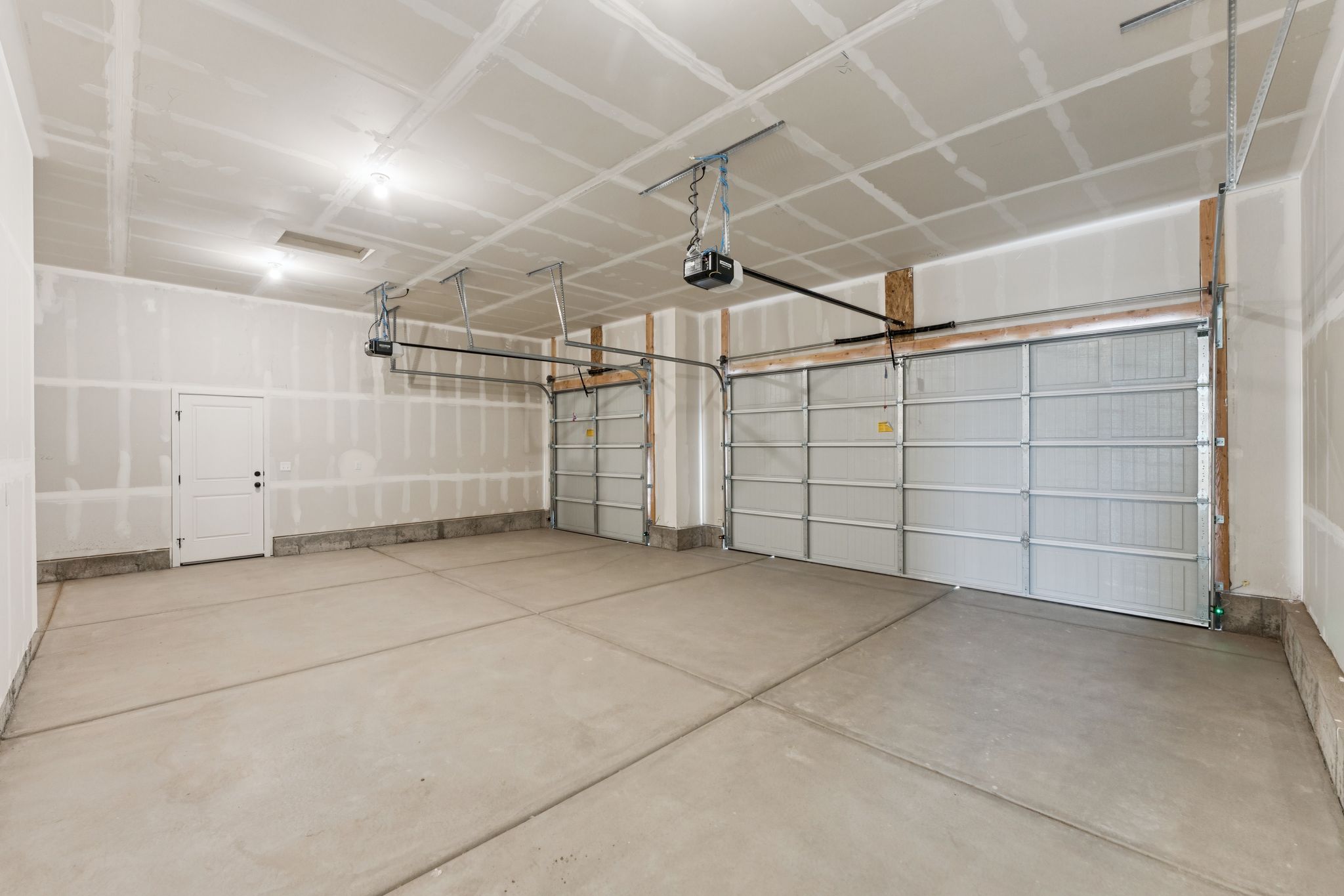 Spacious three-car garage featuring automatic overhead doors, a pedestrian door, and overhead lighting
