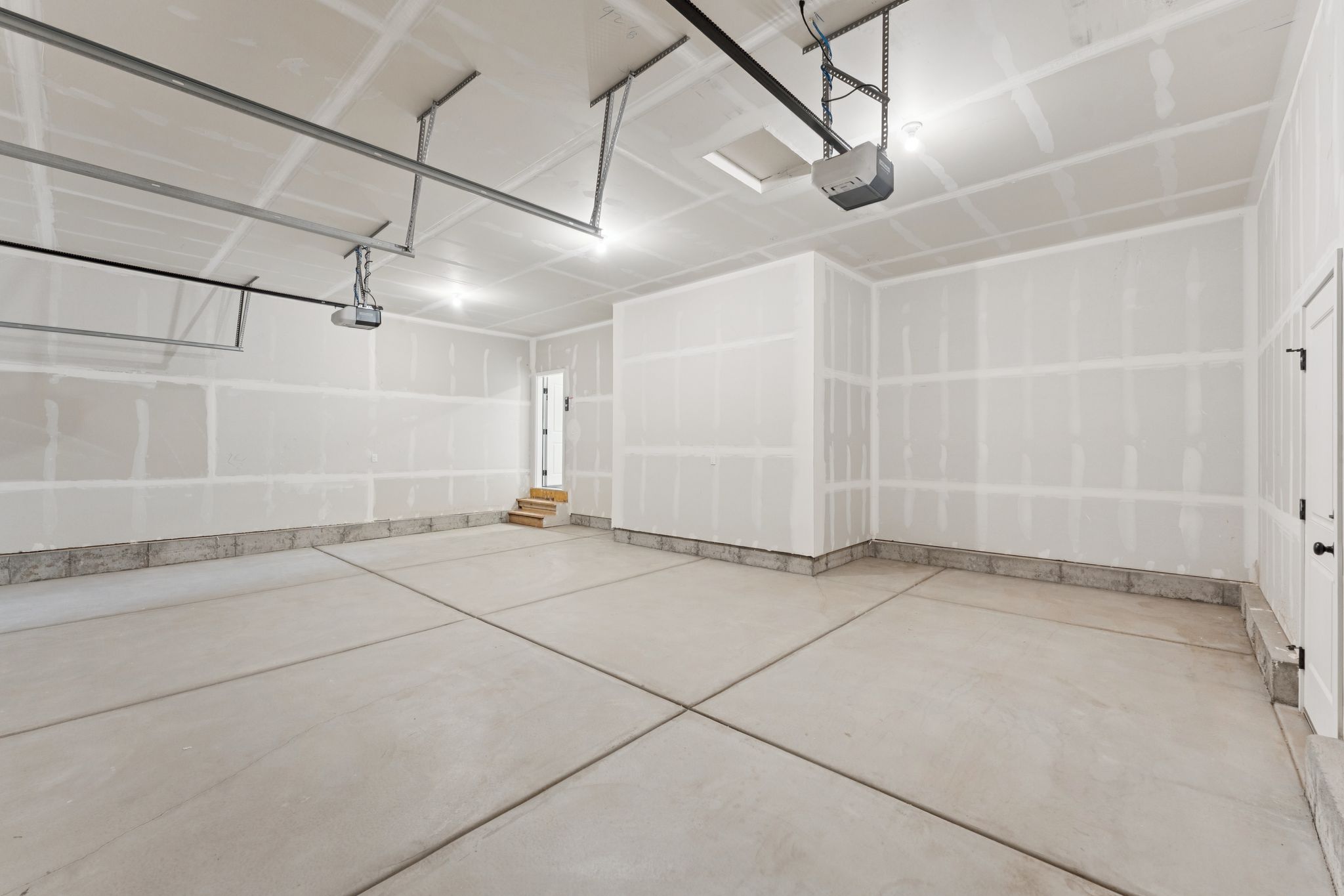 Spacious three-car garage with exposed framing, concrete flooring, and an automatic garage door opener system