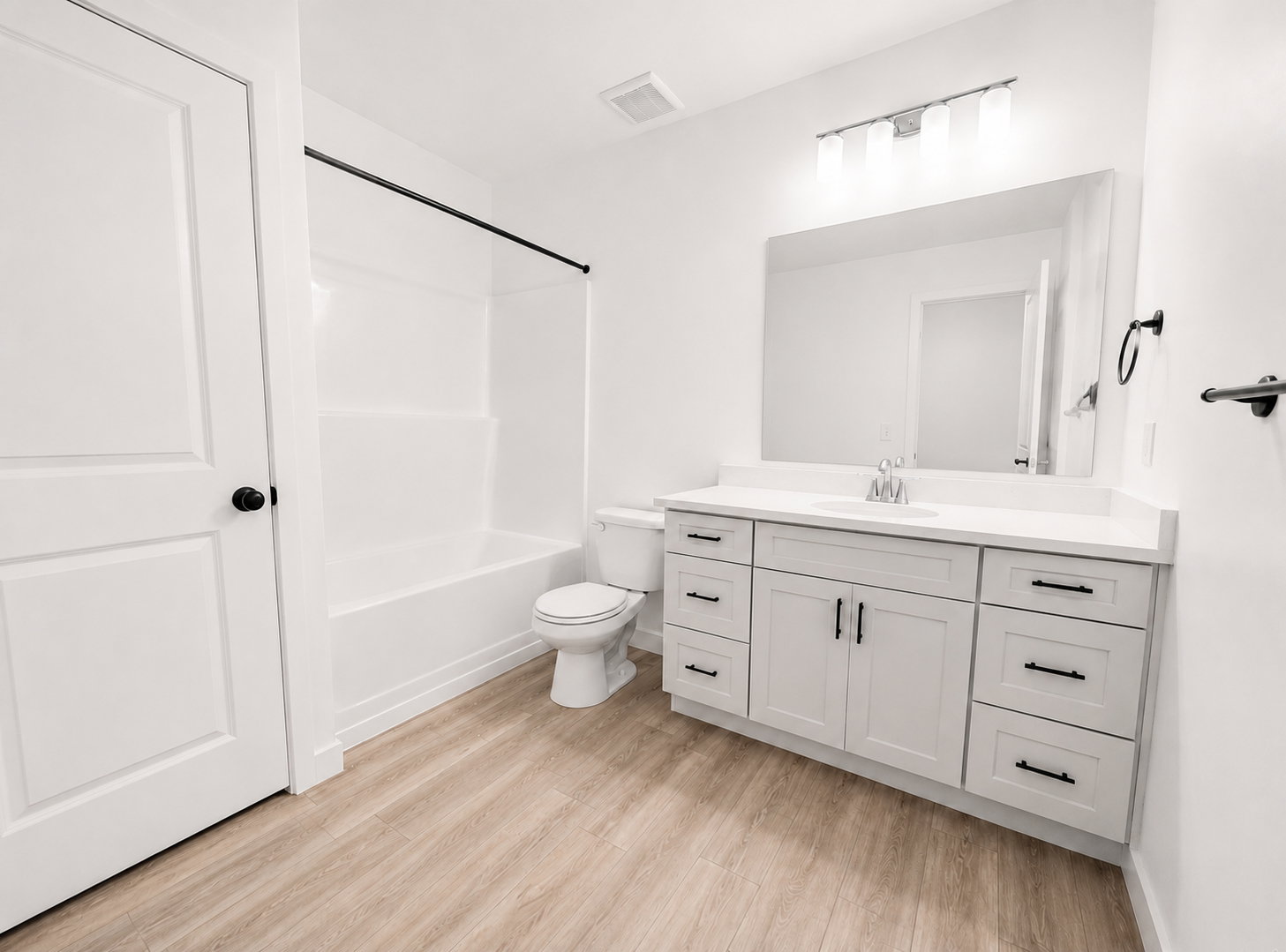 Basement full bathroom featuring a white vanity with a quartz countertop and black hardware, a large mirror, and wood-finish flooring