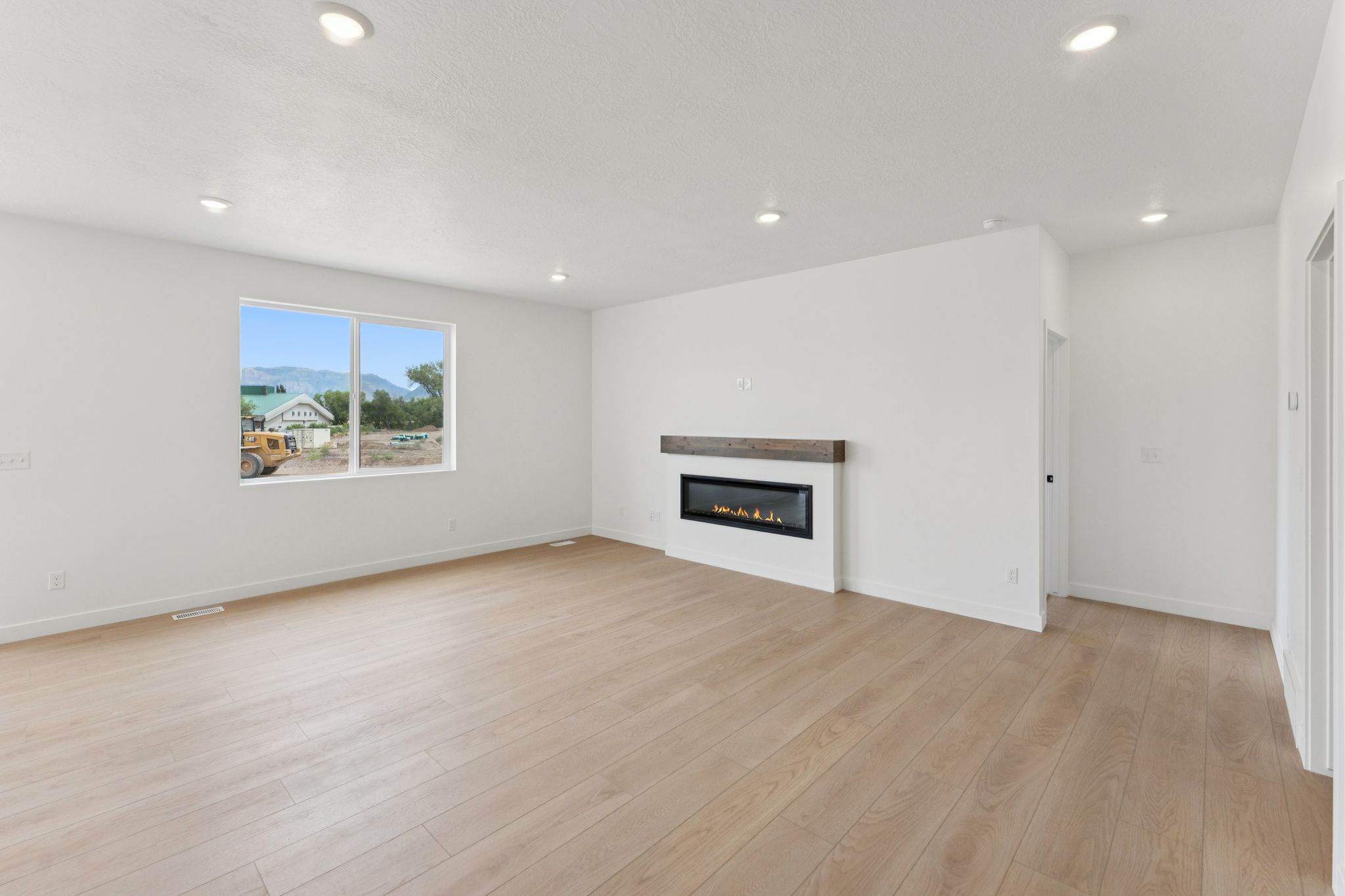 Open-concept living space featuring wood-finish flooring, recessed lighting, and a modern linear fireplace with a stained wood mantel