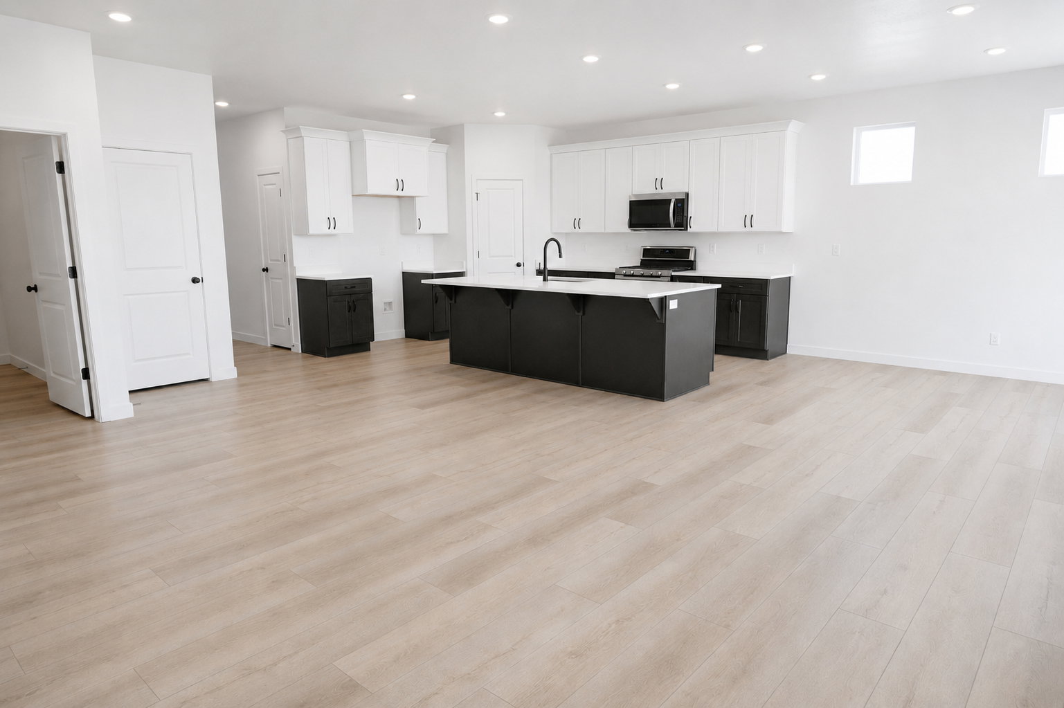 Open-concept kitchen featuring an oversized island with dark cabinetry, stainless steel appliances, light wood-finish flooring, recessed lighting, and white upper and dark lower cabinetry
