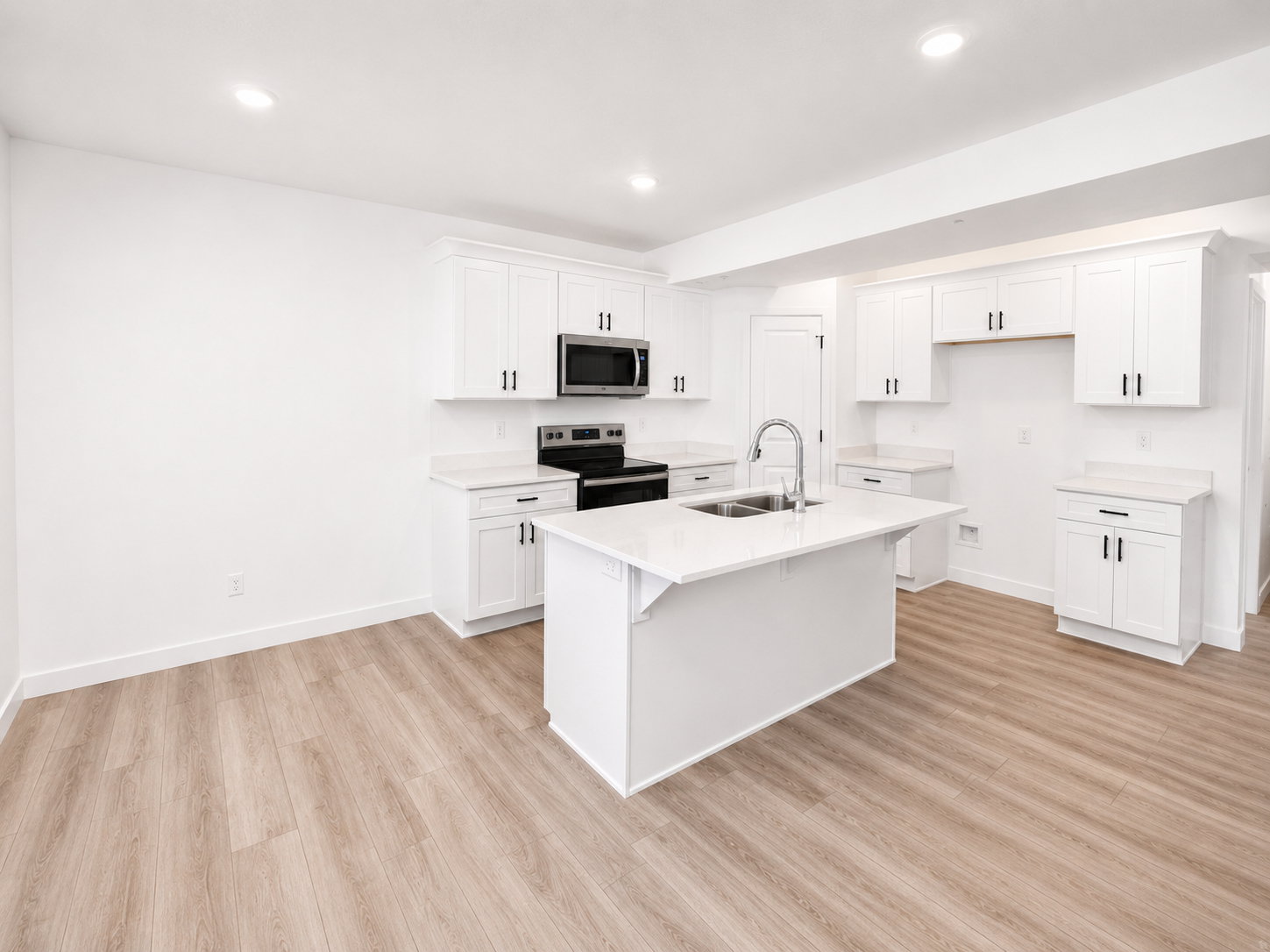 Basement ADU kitchen featuring white shaker cabinetry, light-toned wood-finish flooring, recessed lighting, and a kitchen island with an undermount double-basin sink