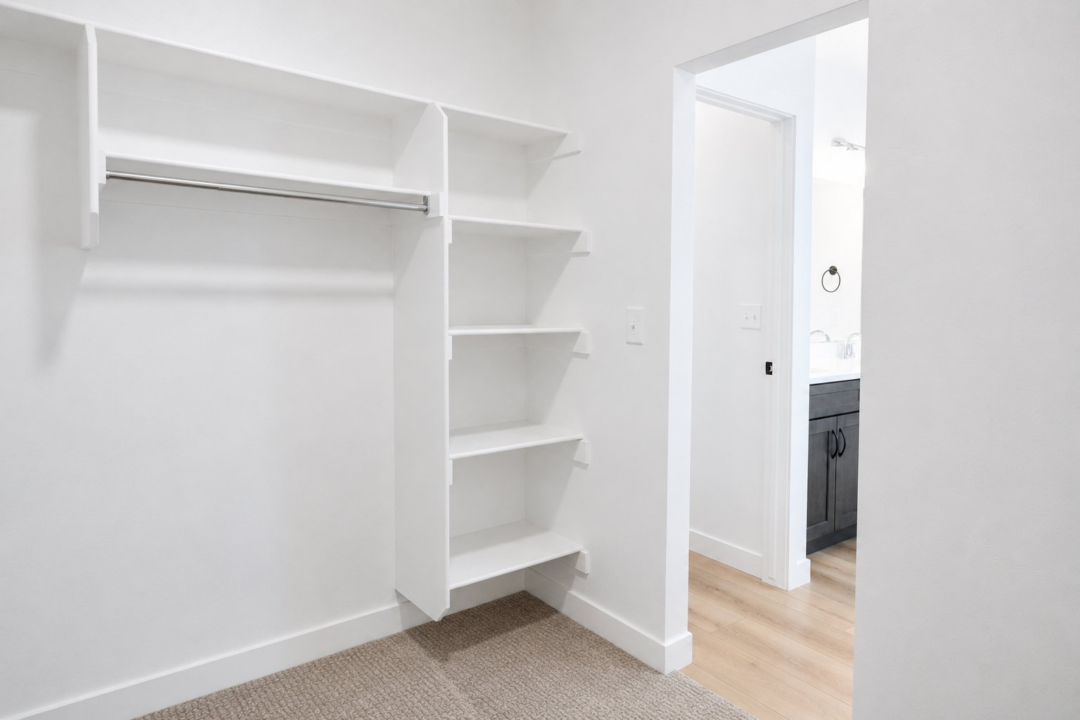 Primary closet featuring built-in white shelving and hanging rod with carpeted flooring
