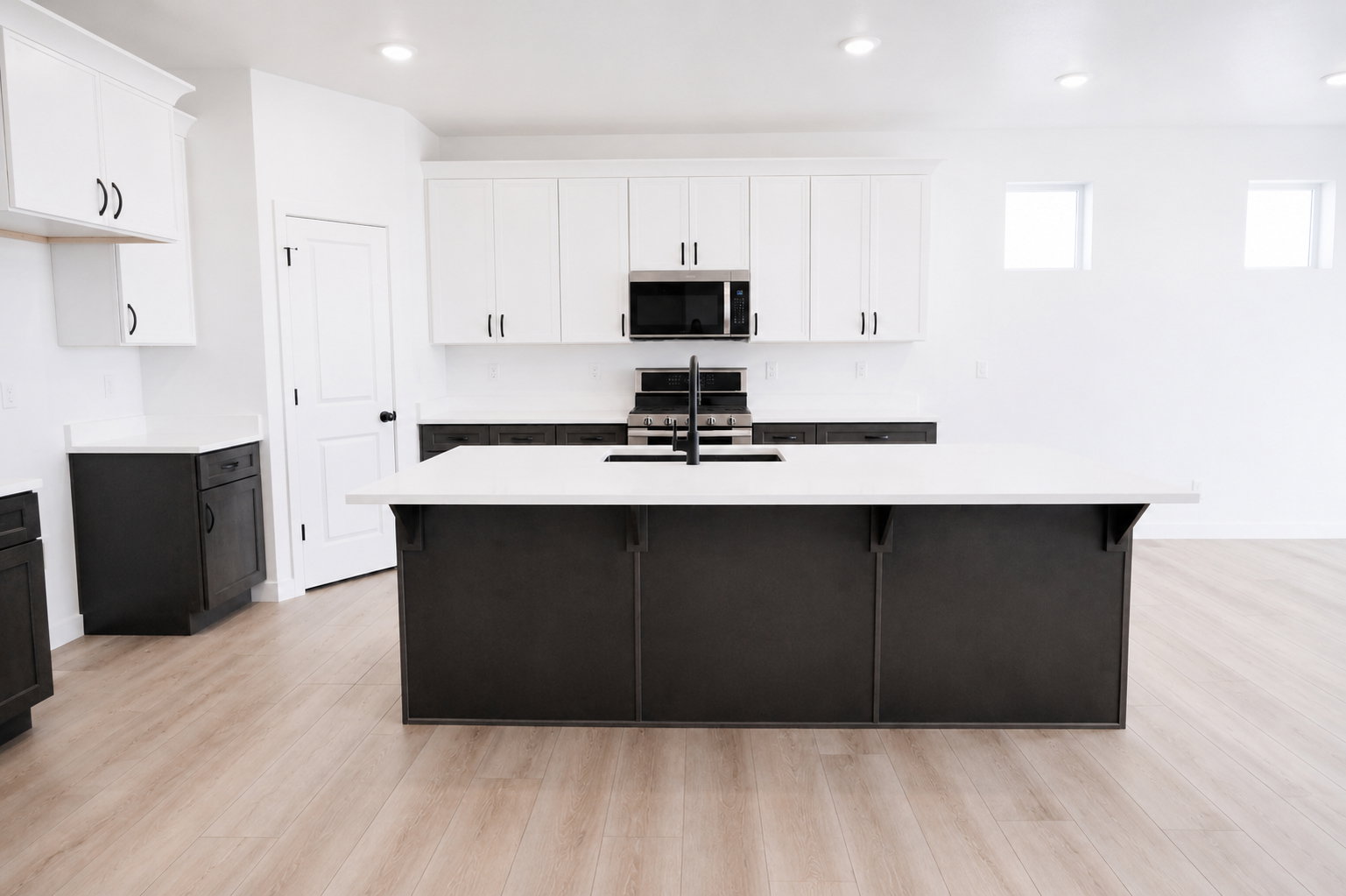 Spacious kitchen featuring a central island with quartz countertops and integrated sink, light wood-finish flooring, two-tone cabinetry with white upper and dark lower units, stainless steel appliances, and recessed lighting