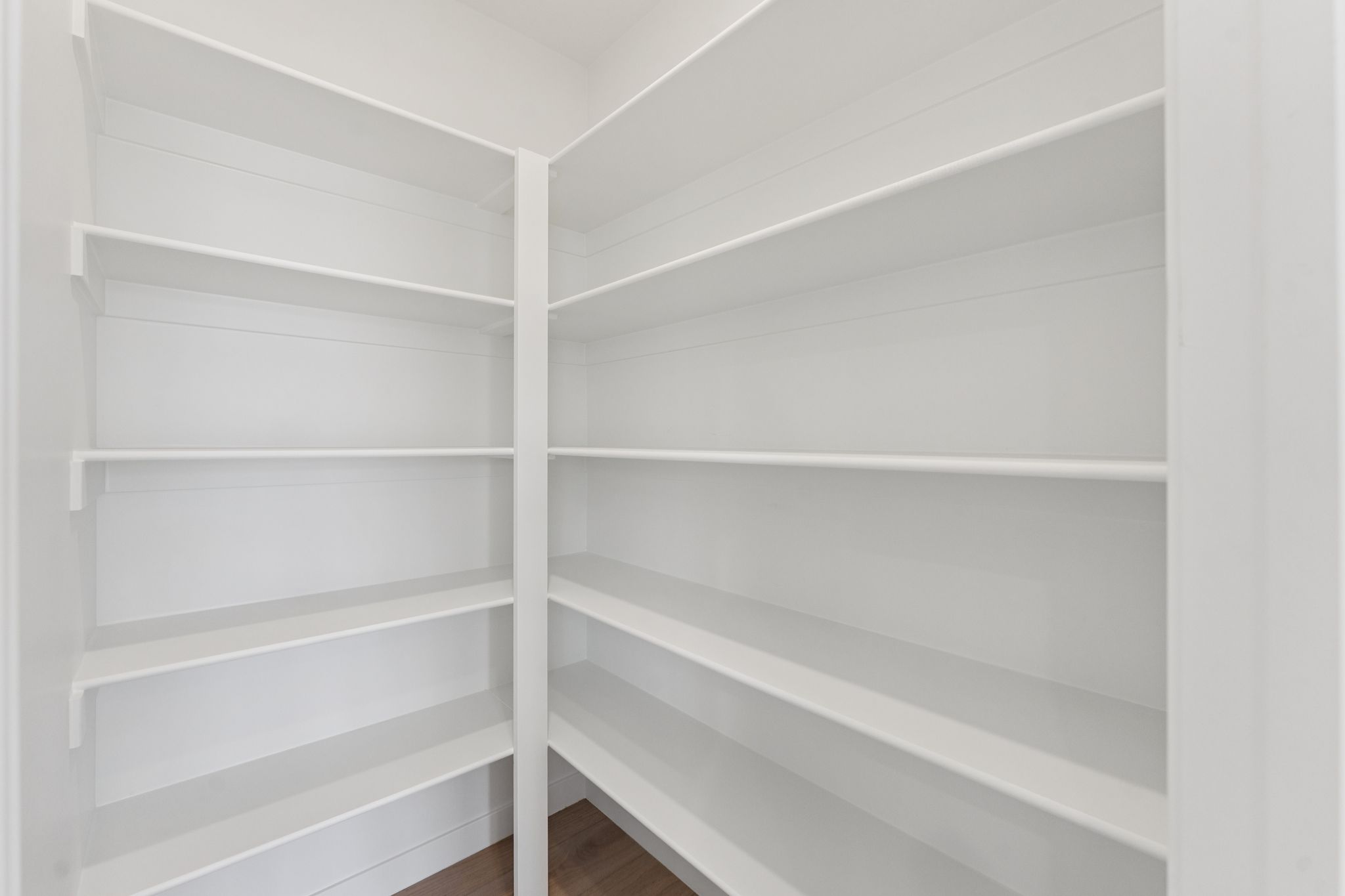 Spacious pantry featuring multiple tiers of white shelving and wood-finish flooring