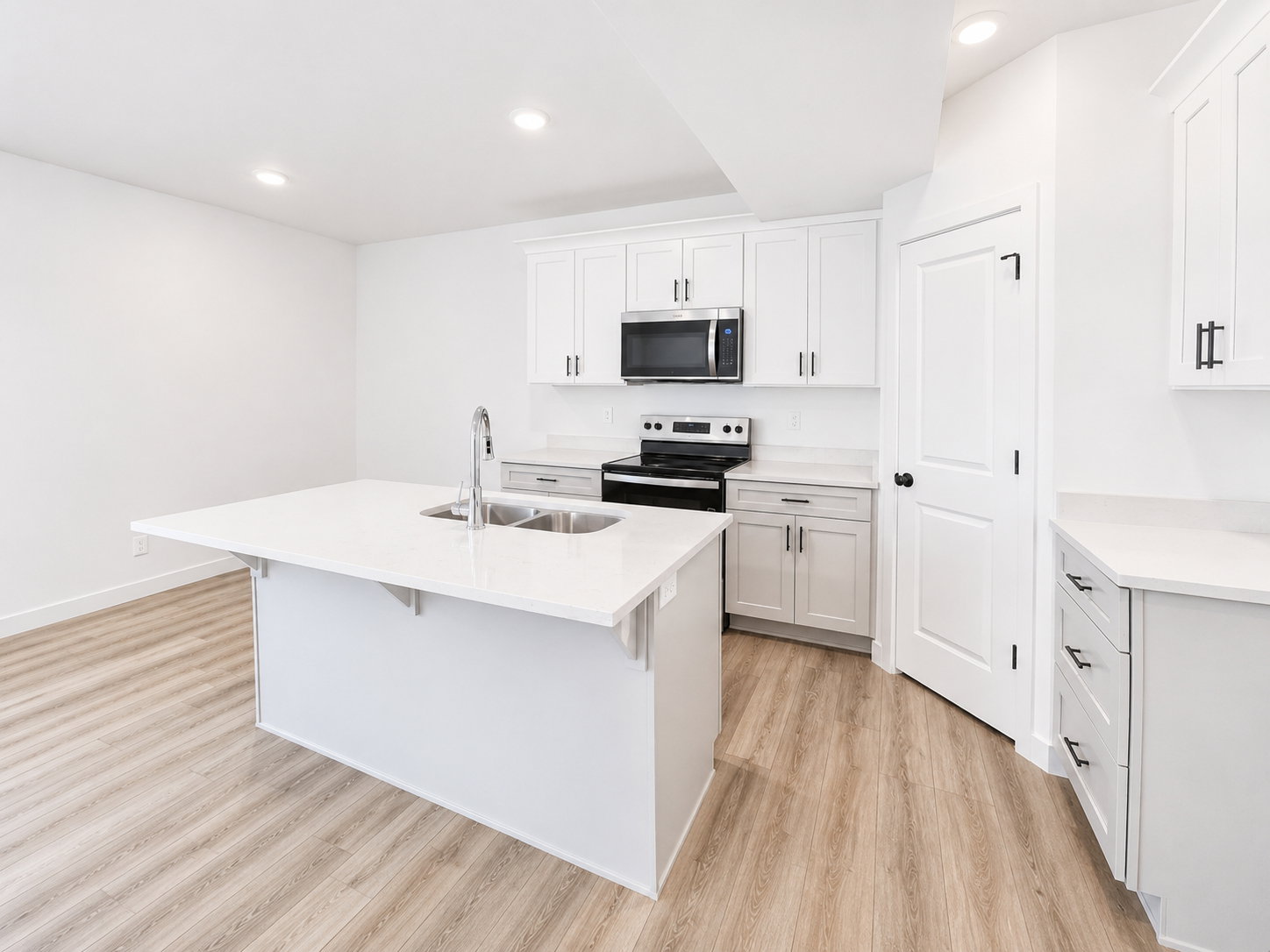 Basement ADU kitchen featuring white shaker cabinetry, light-toned wood-finish flooring, recessed lighting, and a kitchen island with an undermount double-basin sink