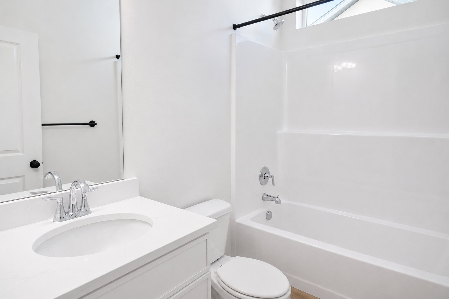 Main floor bathroom featuring a white vanity with an integrated sink, polished chrome faucet, a standard toilet, and a white tub/shower combination with chrome fixtures
