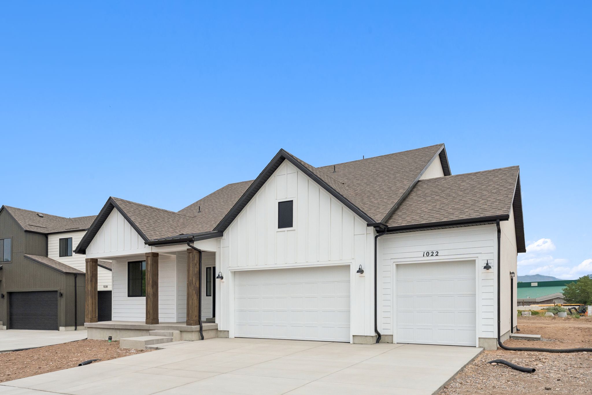Modern farmhouse exterior featuring white board and batten siding, dark trim accents, and a covered porch with wood wrapped columns
