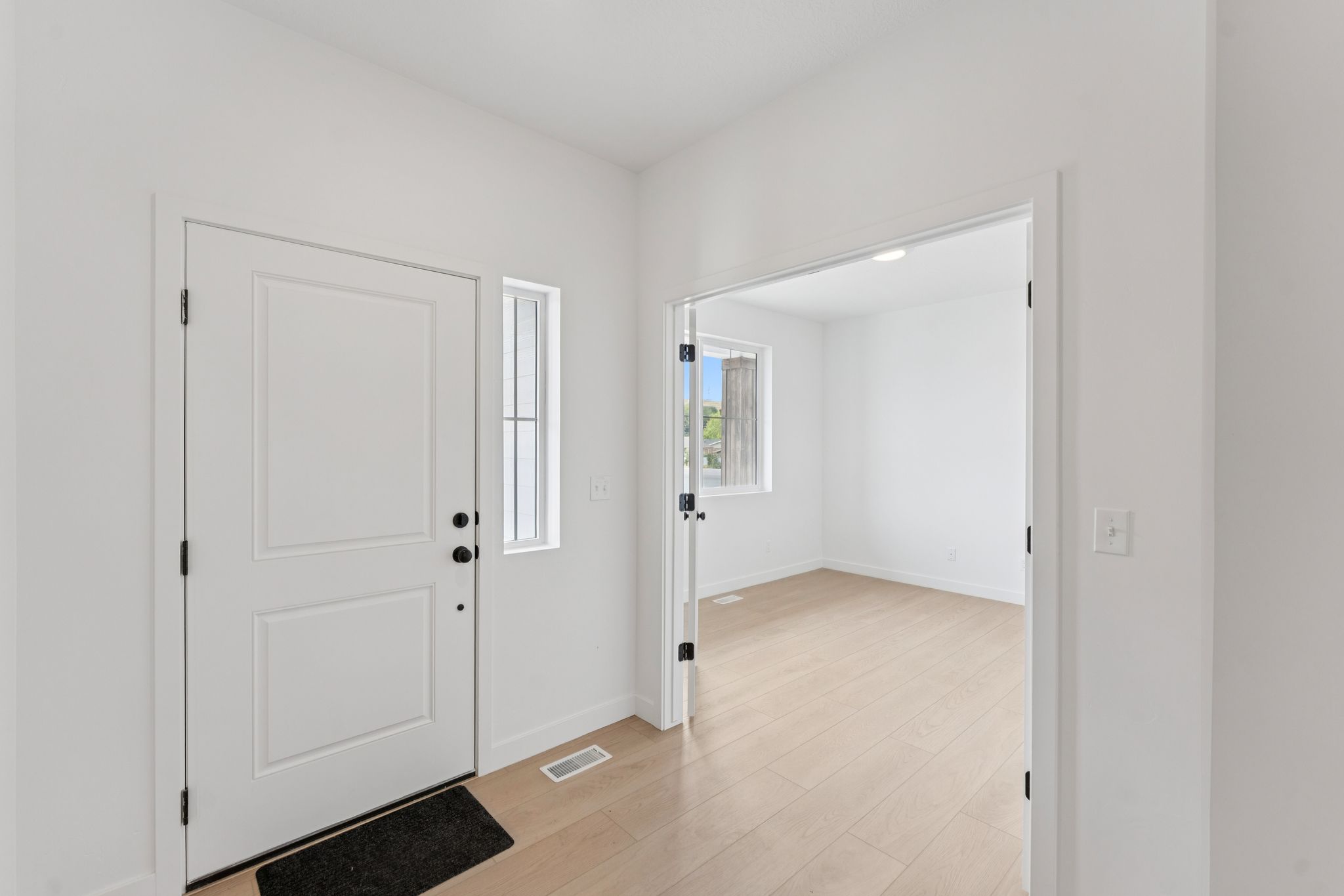 Entryway featuring a paneled door with black hardware and light wood-finish flooring extending into a main floor office