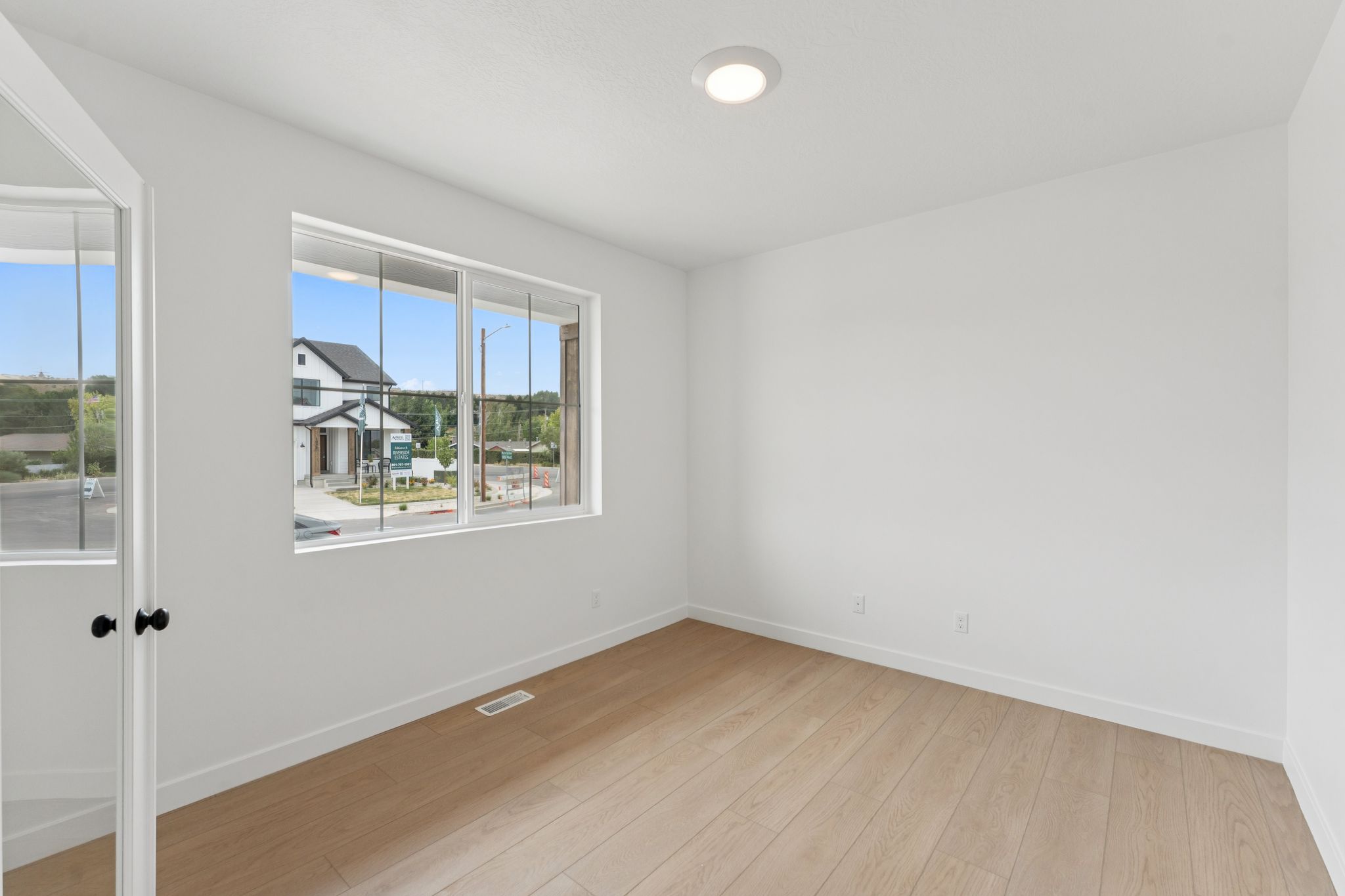 Main floor office featuring a large window, light wood-finish flooring, white walls, and a ceiling-mounted light fixture