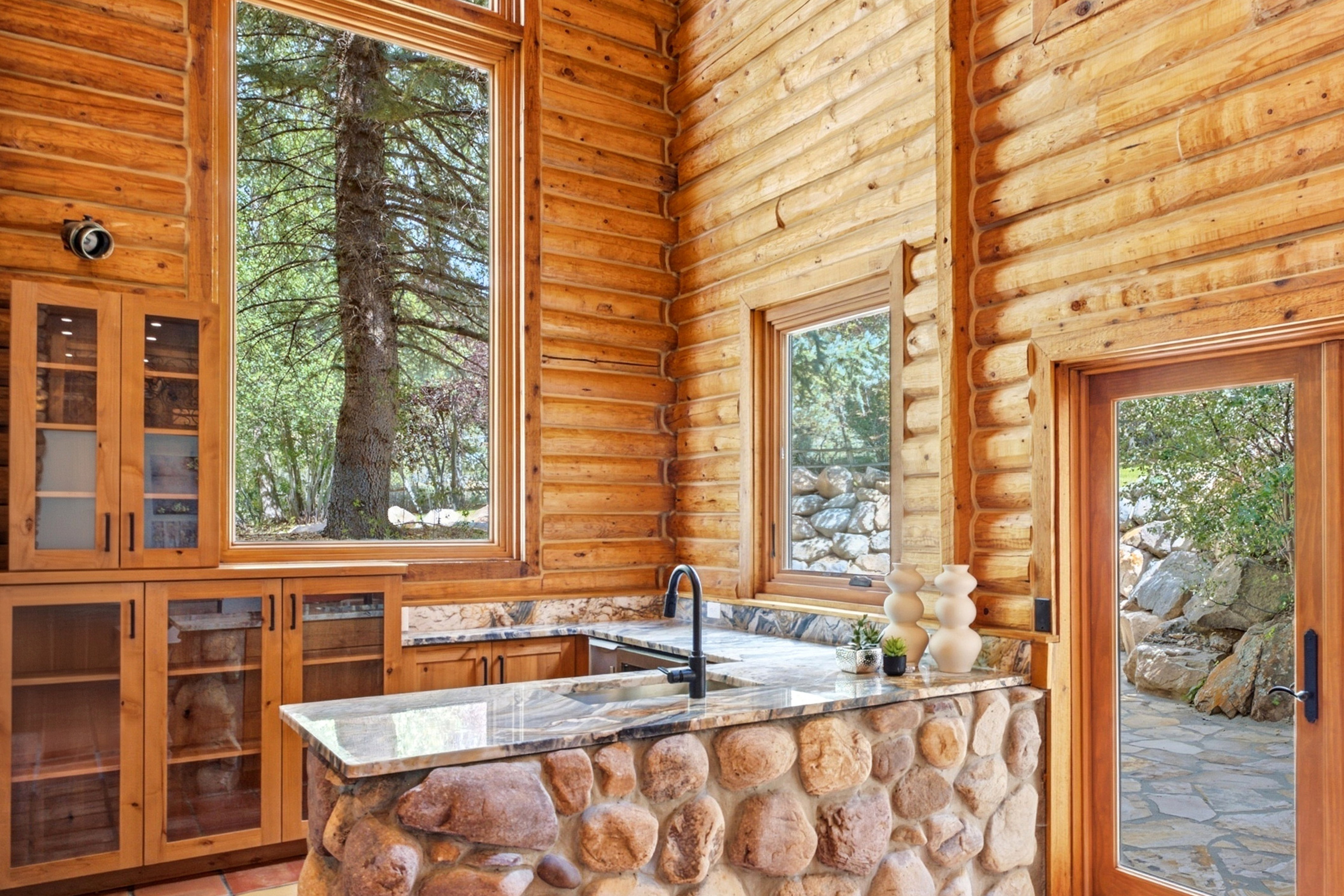Double-height log walls featuring a stone-clad kitchen island with a built-in sink and dark-finish faucet