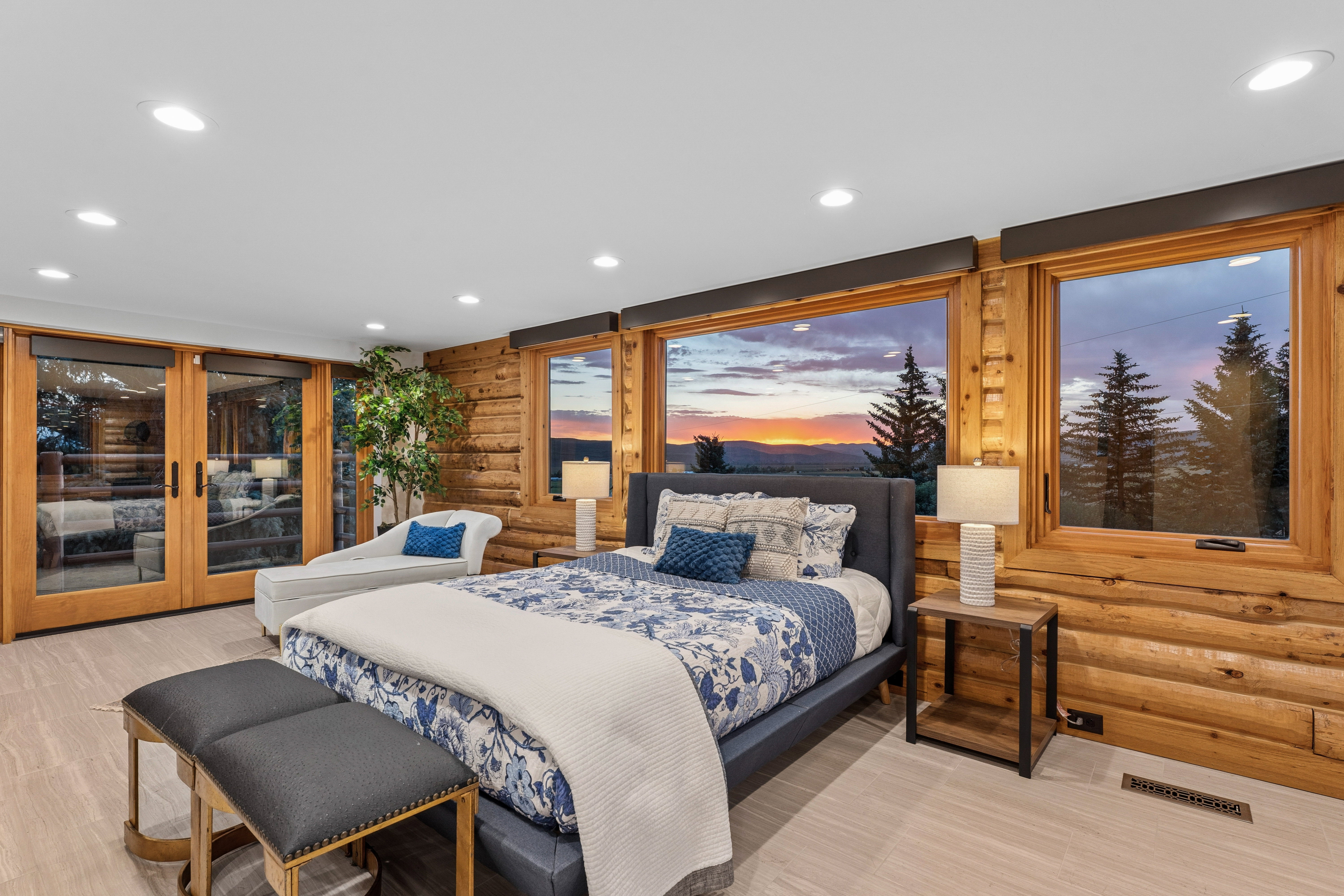Bedroom featuring log wall construction, light wood-finish flooring, recessed ceiling lighting, and large windows with outdoor scenery