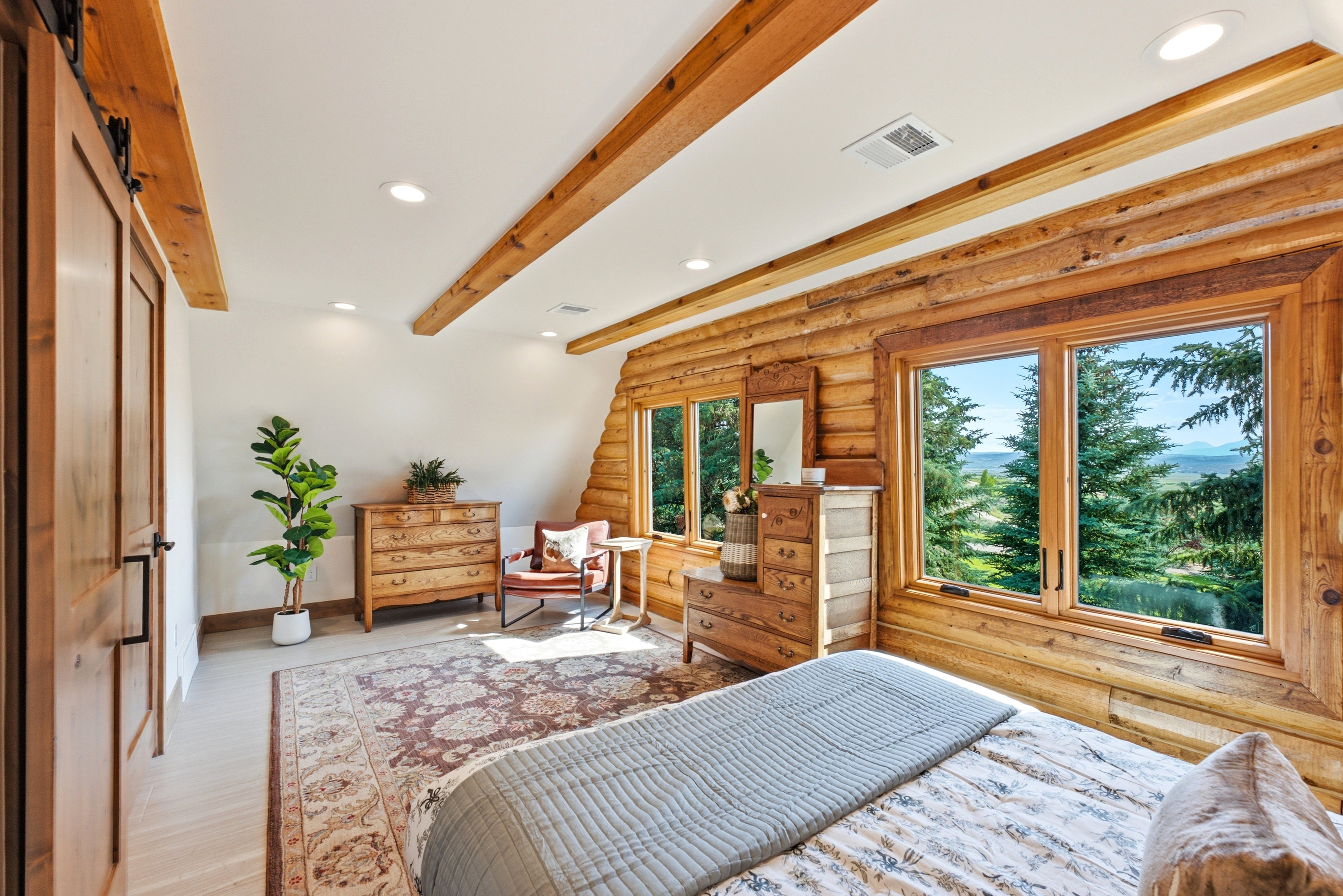 Expansive windows offering a scenic outdoor panorama, complemented by natural wood log walls and exposed ceiling beams