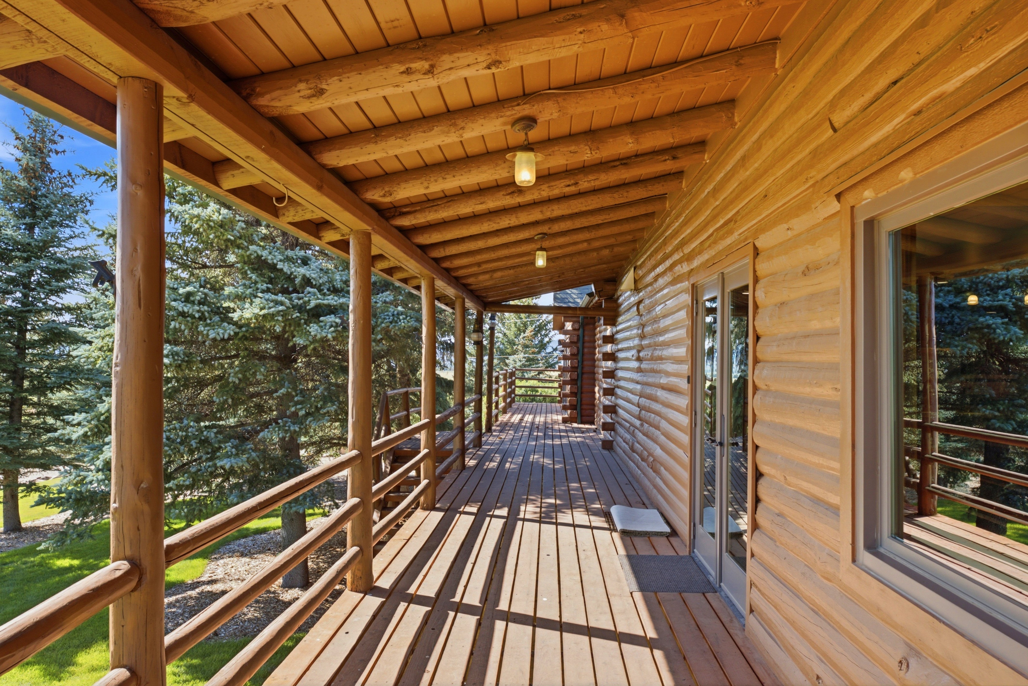 Expansive wood-finish deck with log railing, a log-style overhang, exposed wood ceiling beams, and exterior log siding