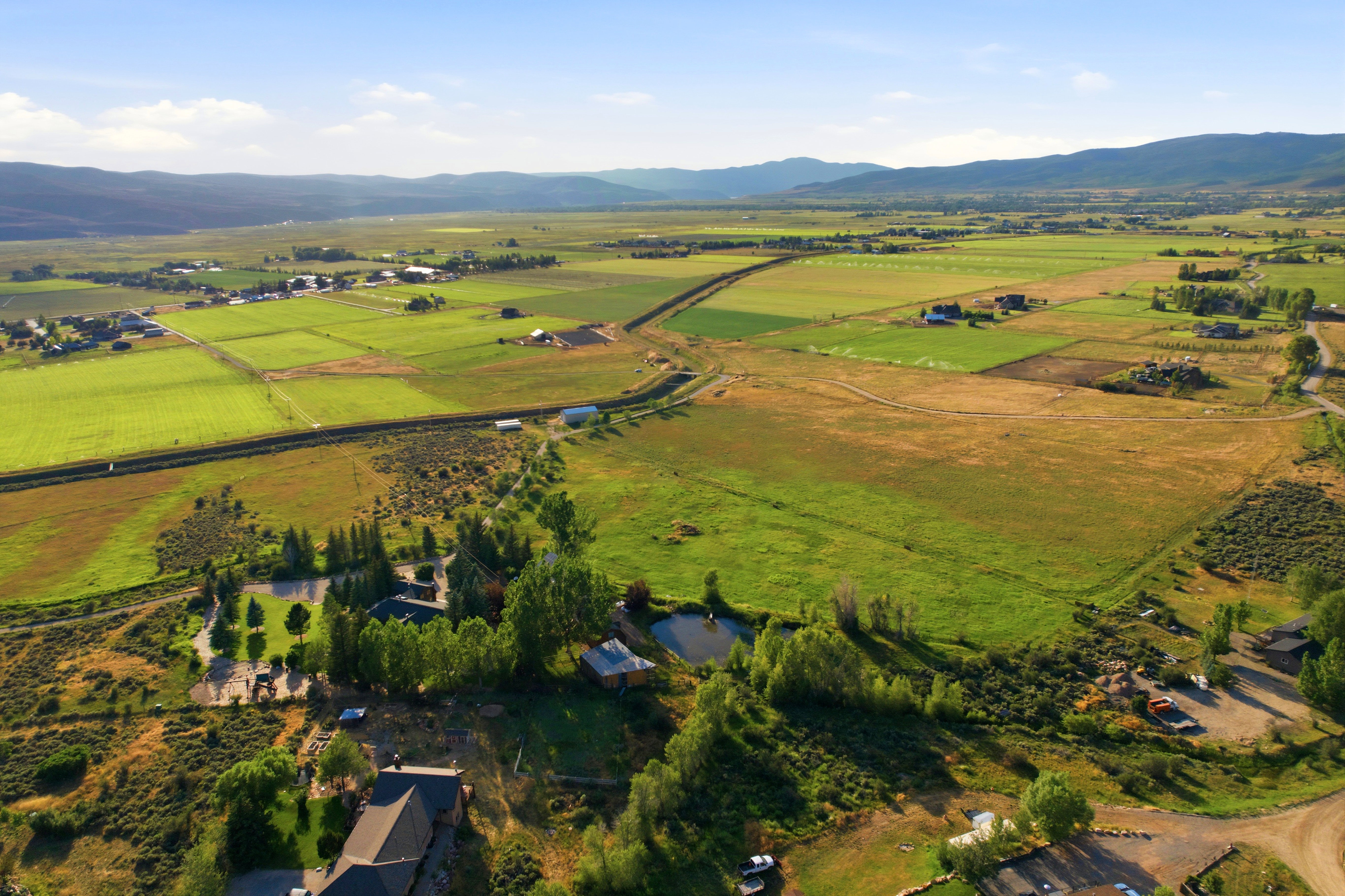 Expansive aerial landscape featuring extensive green fields, distant mountain ranges, and numerous residential structures
