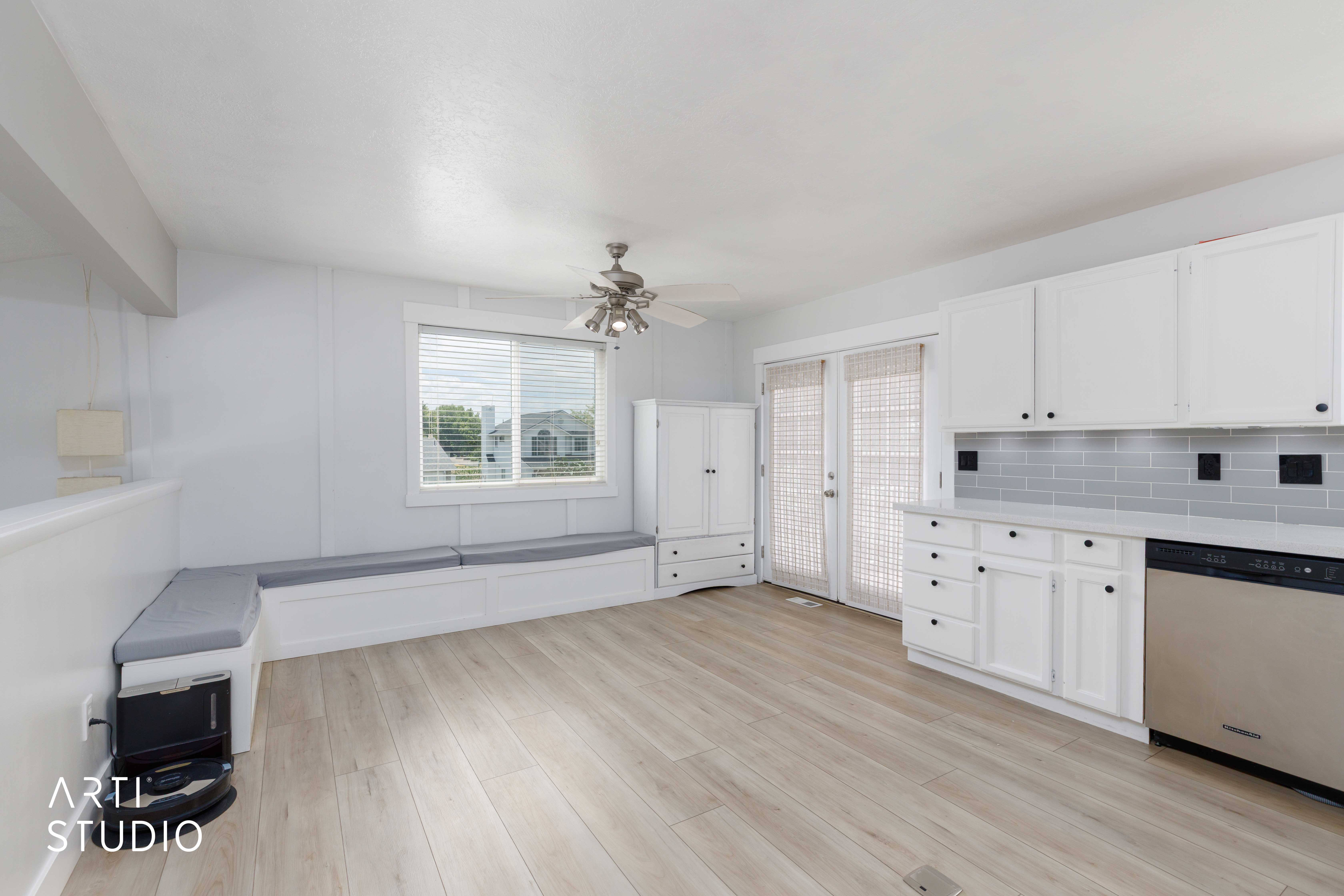 Open-concept space featuring light wood-finish flooring, white cabinetry with black hardware, a subway tile backsplash, and a built-in window bench with cushions