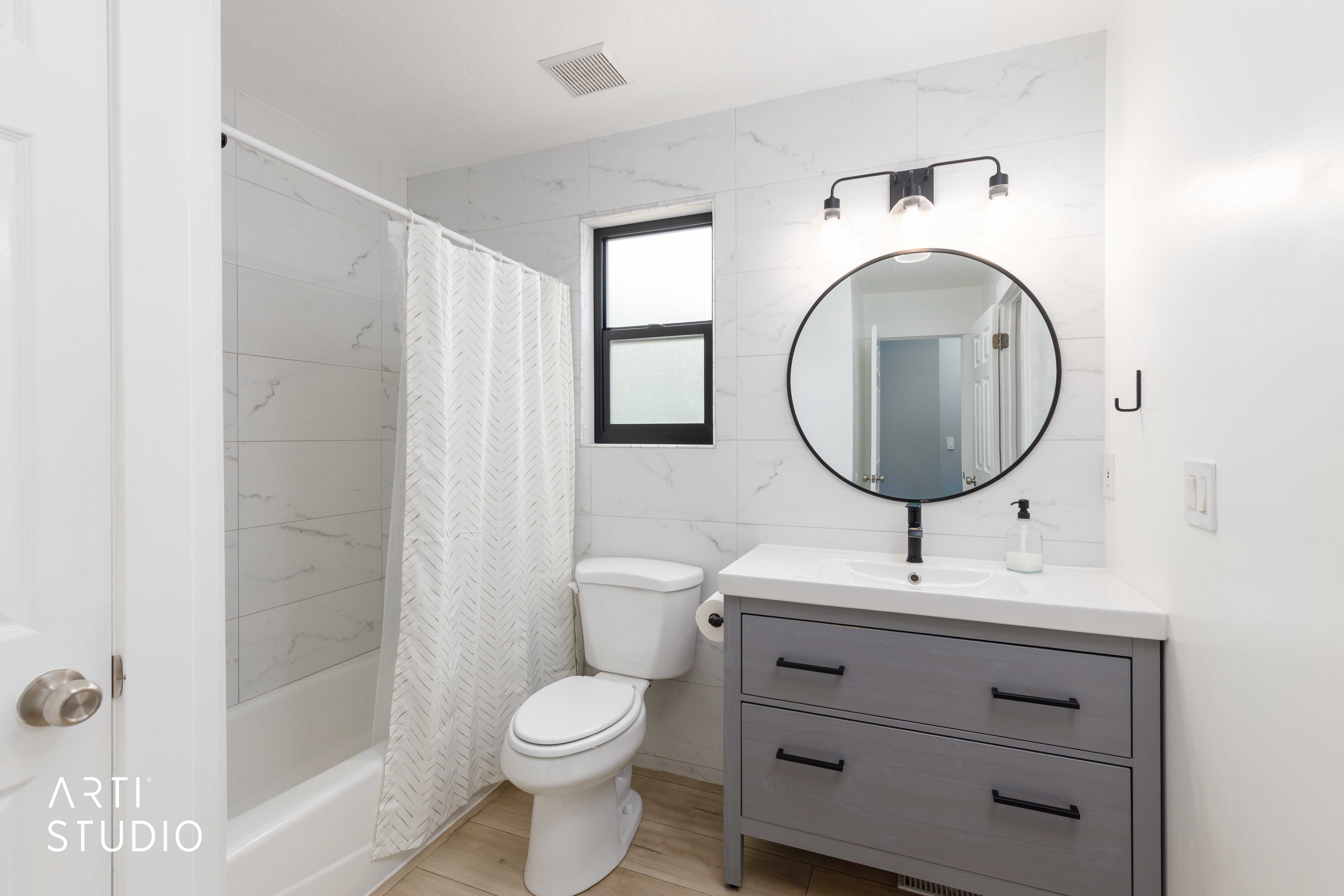 Bathroom featuring a single vanity with a white countertop, round mirror, and matte black lighting fixture