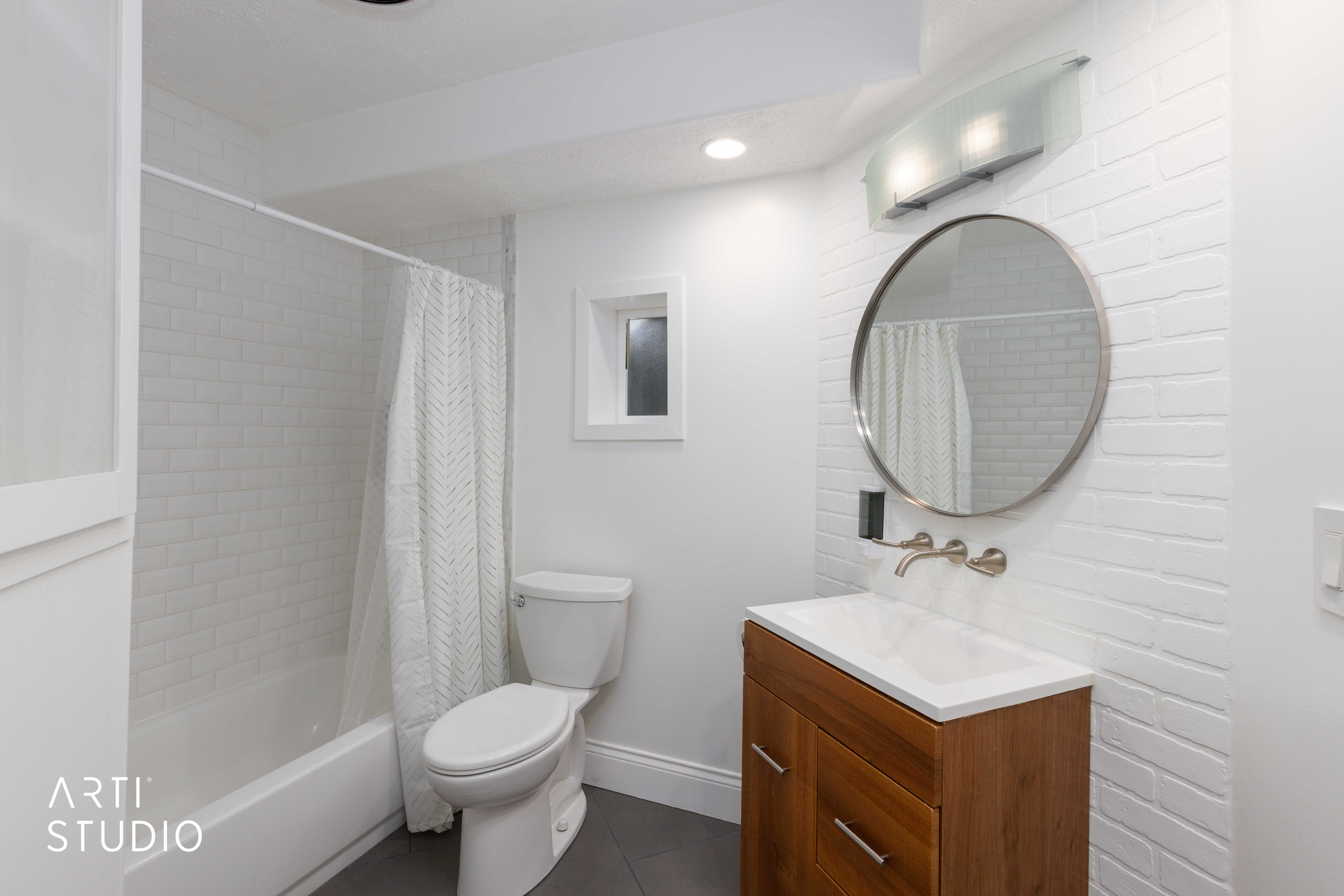 Modern bathroom featuring a wood-finish vanity with an integrated sink, a circular mirror, and a wall-mounted faucet