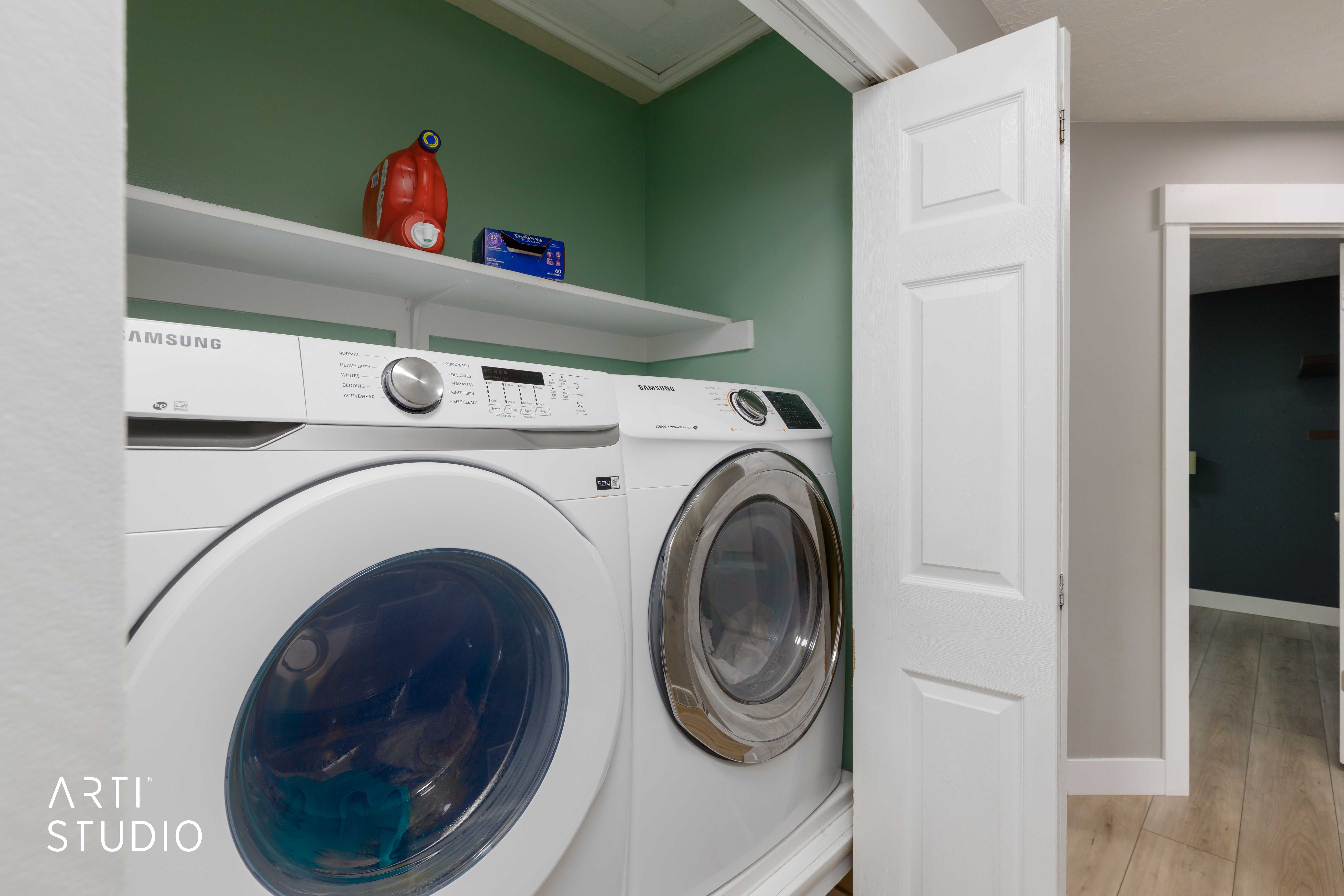 Dedicated laundry area with built-in shelving, a neutral green wall finish, and a white paneled bi-fold door