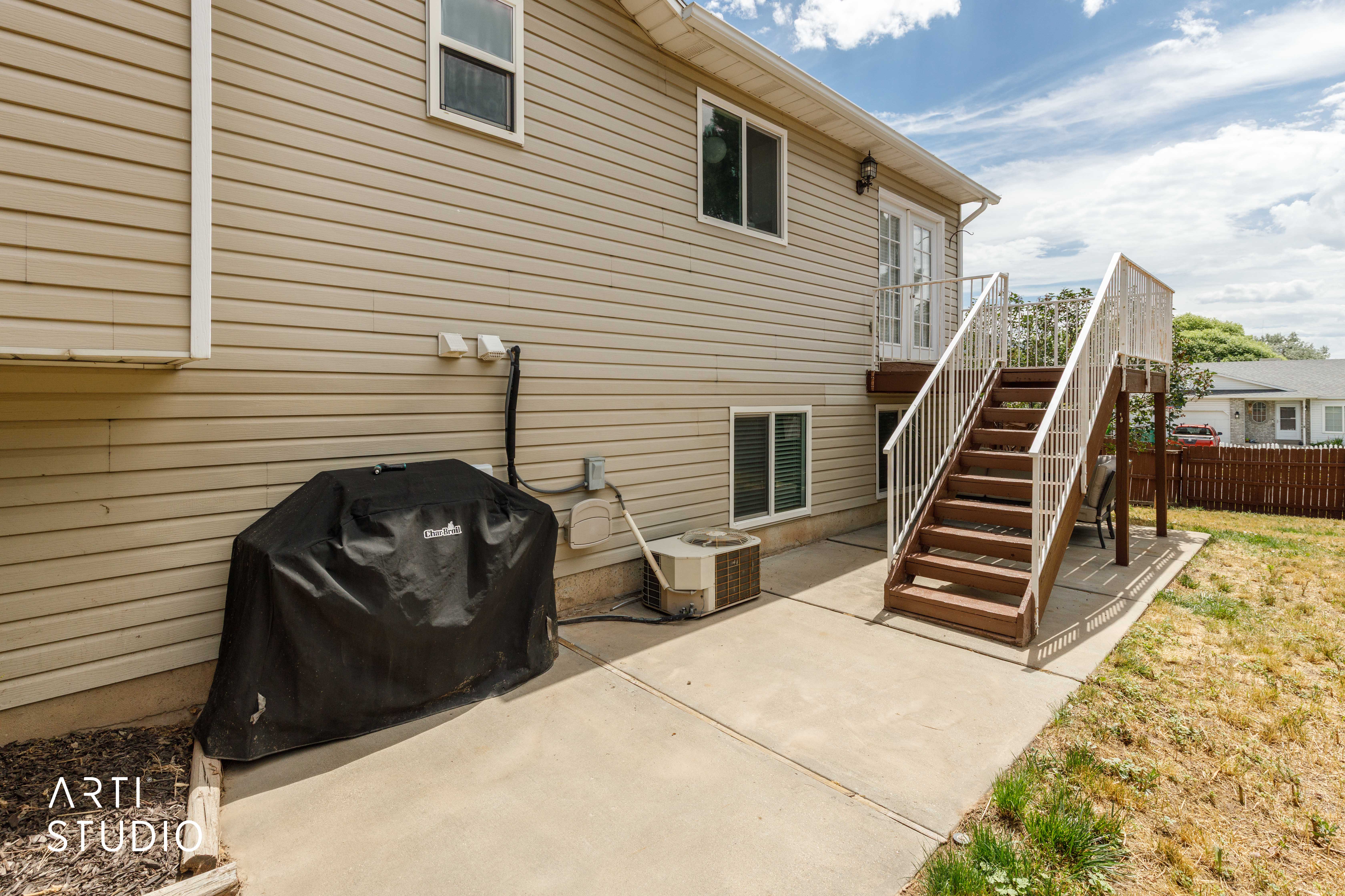 Exterior featuring tan horizontal siding, a concrete patio, and a wood-finish staircase with white railings leading to a second-story entry