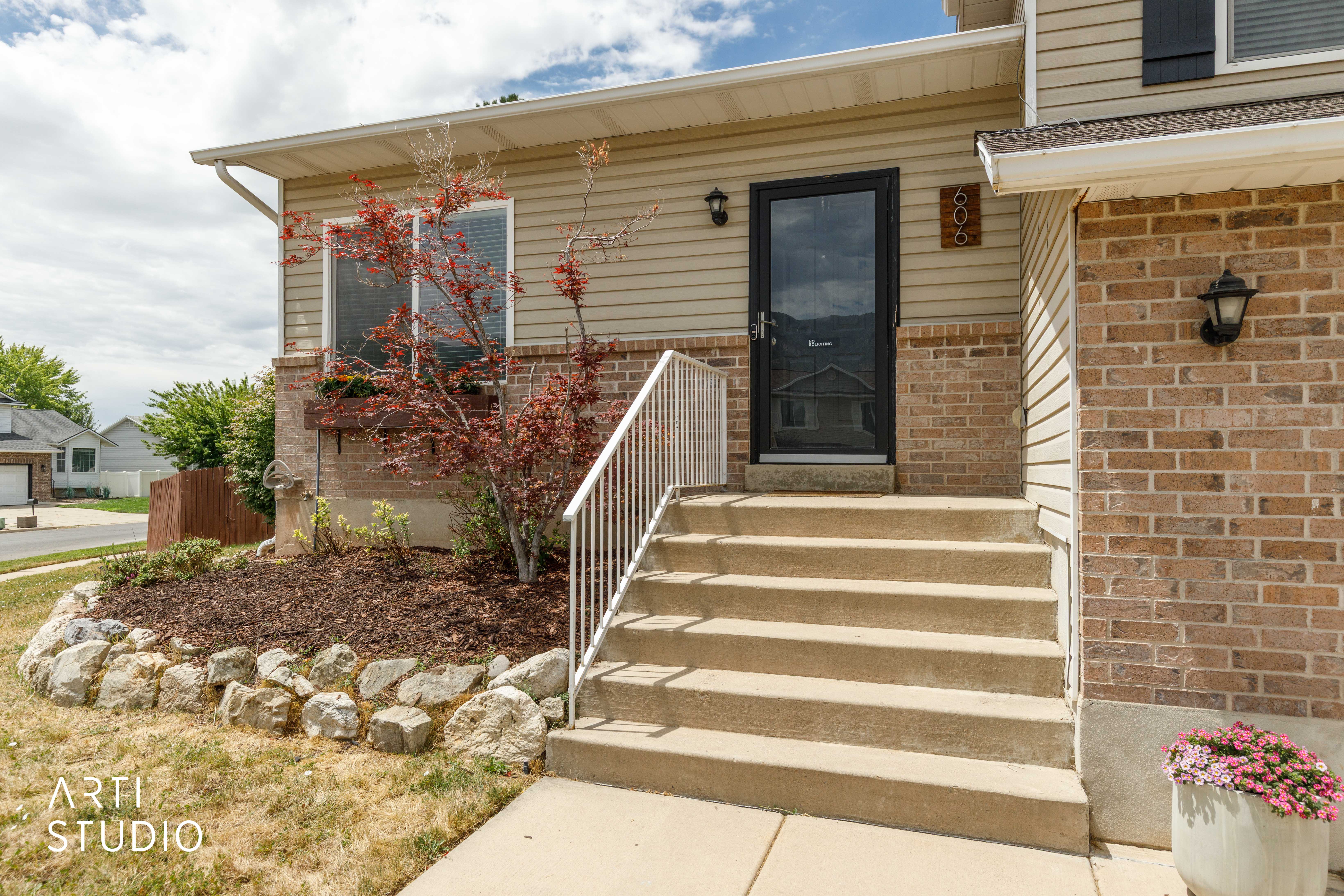 Brick and siding exterior featuring a concrete staircase with white railings, a dark storm door, and a recessed window with a window box
