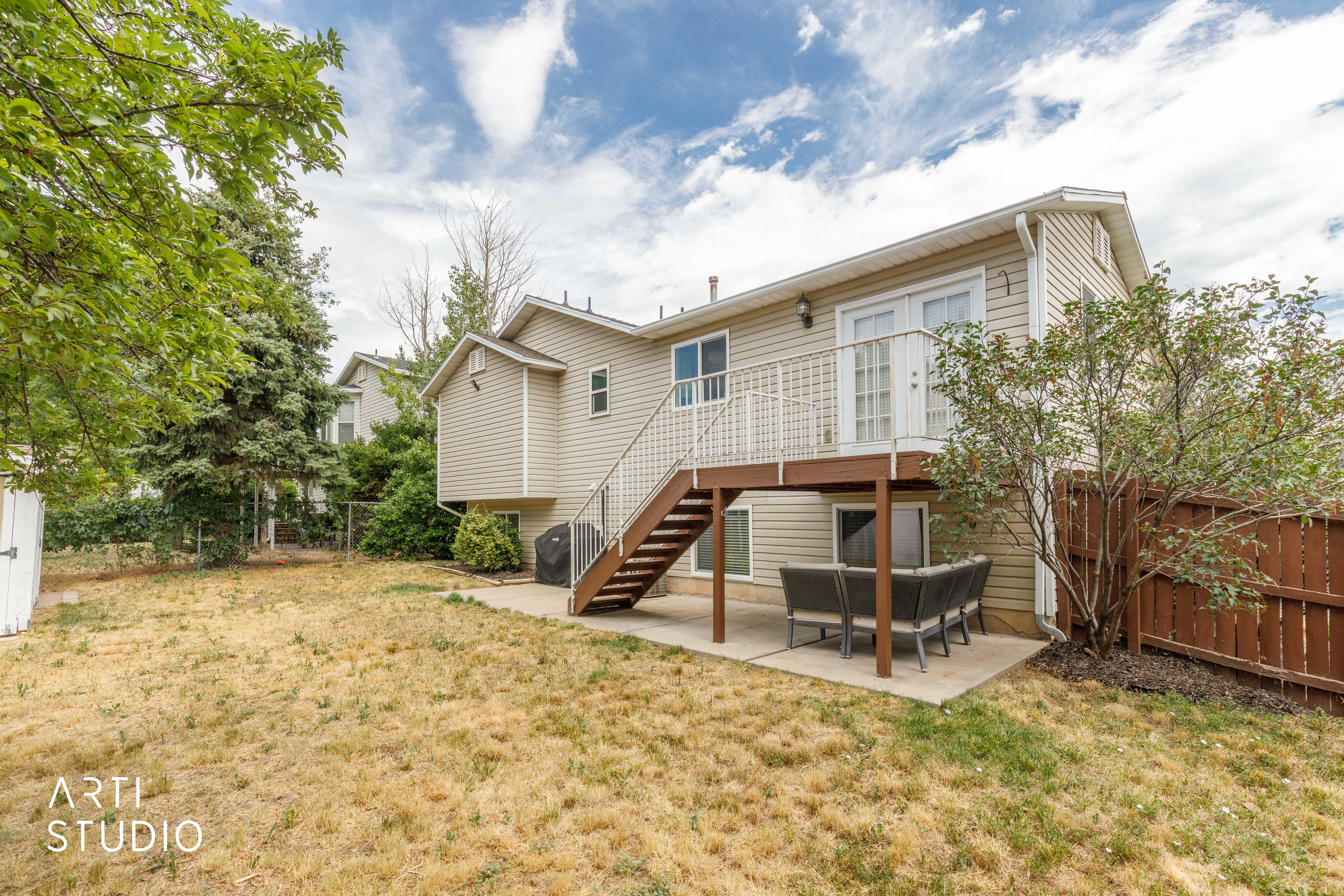 Rear exterior featuring a raised wooden deck with white railings, direct access via patio doors, and a concrete patio below