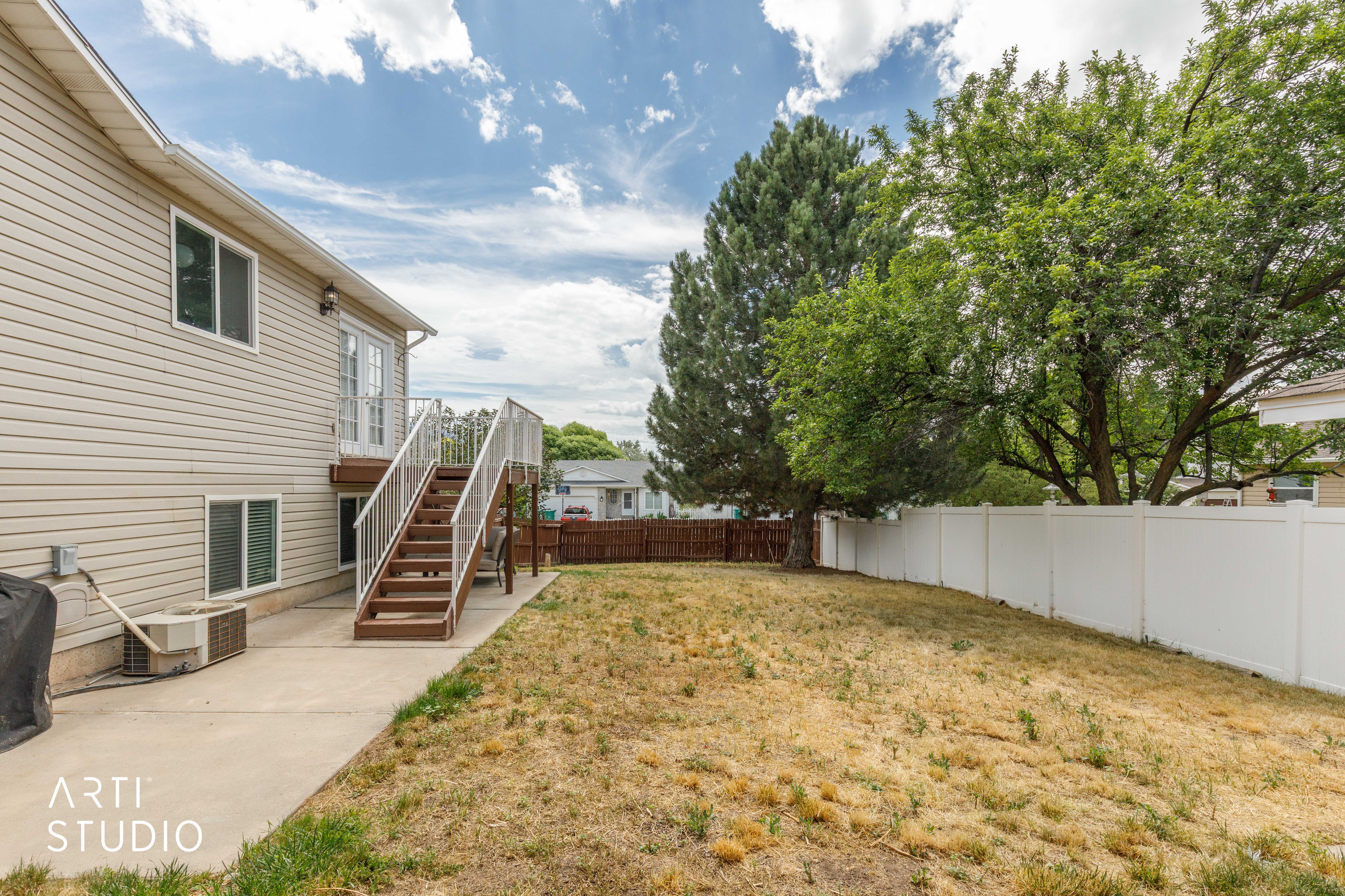 Rear exterior featuring a concrete patio, wood-finish exterior staircase with white railings, and sliding glass doors