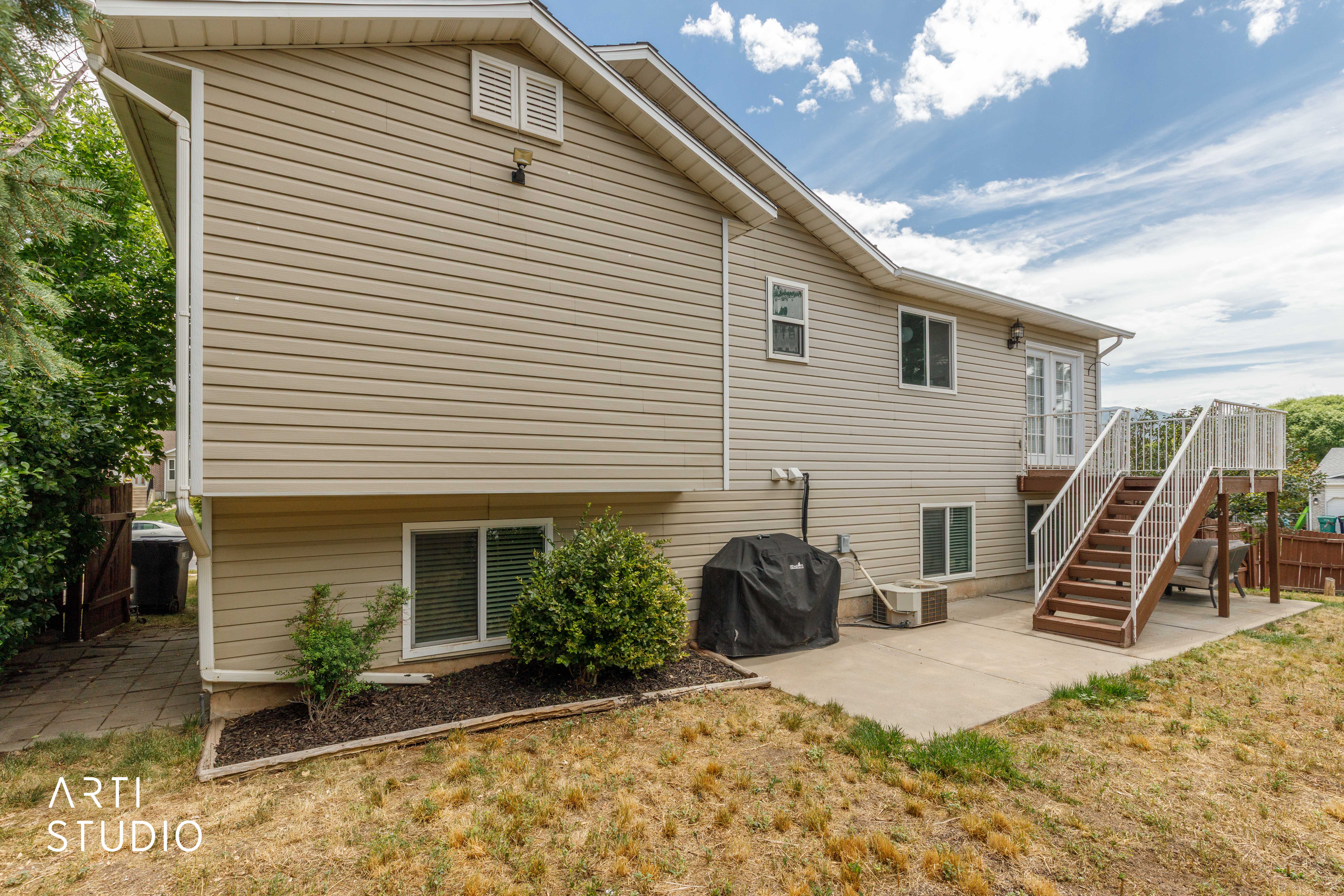 Rear elevation featuring tan siding, a ground-level concrete patio, and a brown wood deck with white railings