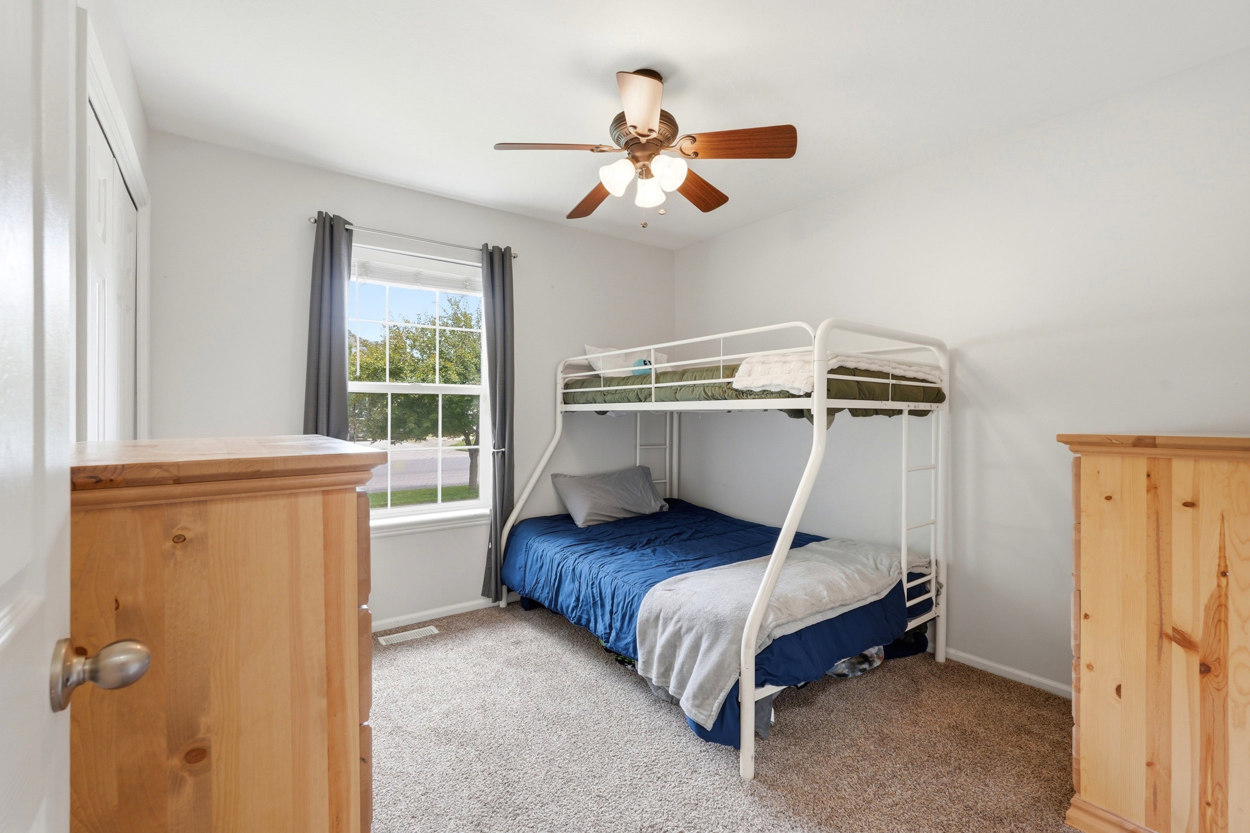 Bright room featuring a ceiling fan with integrated lighting, a double-hung window with a street-facing orientation, light-colored walls, and carpeted flooring