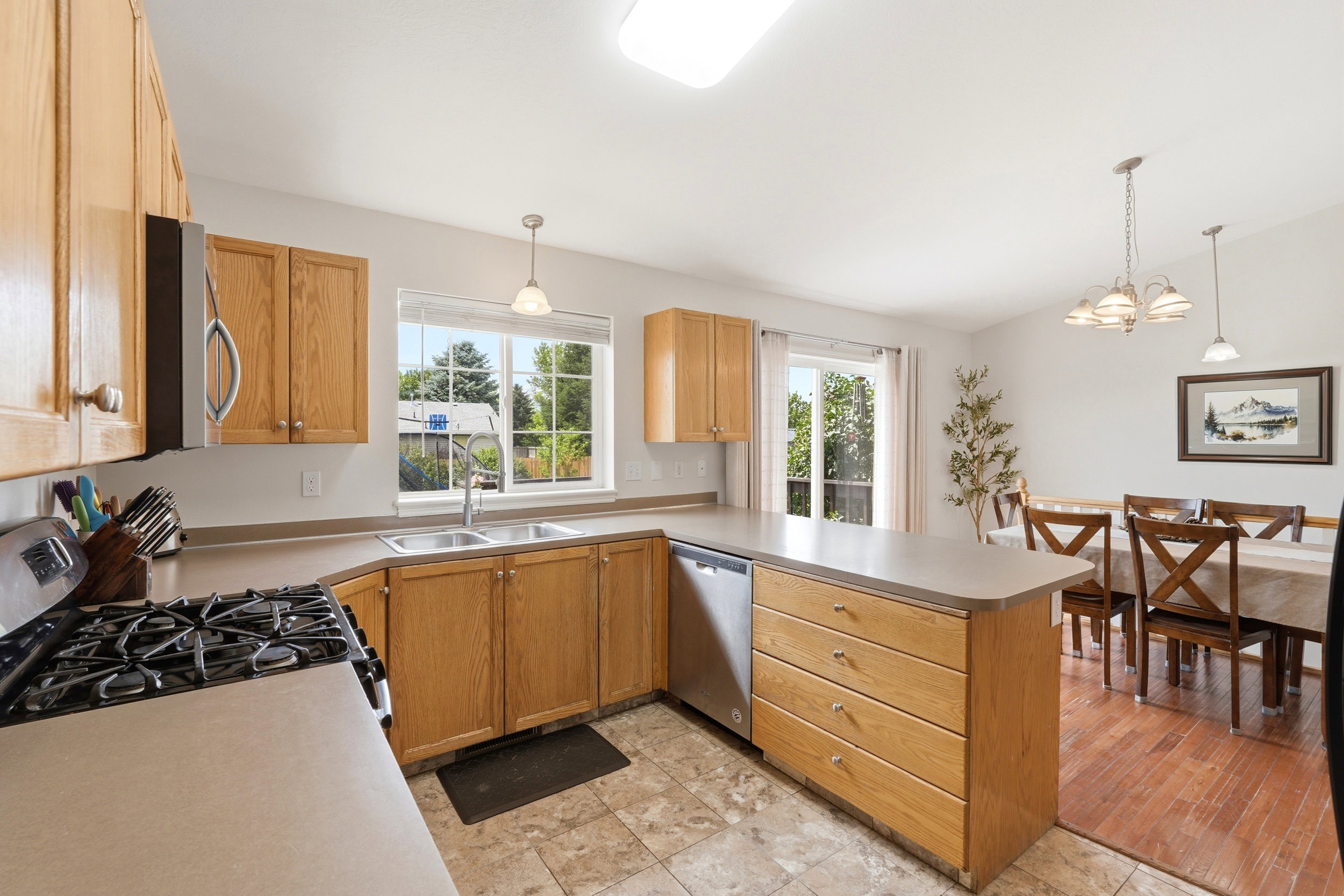 Kitchen featuring wood-finish cabinetry, neutral countertops, a gas range, a stainless steel microwave, and a double basin sink beneath a large window