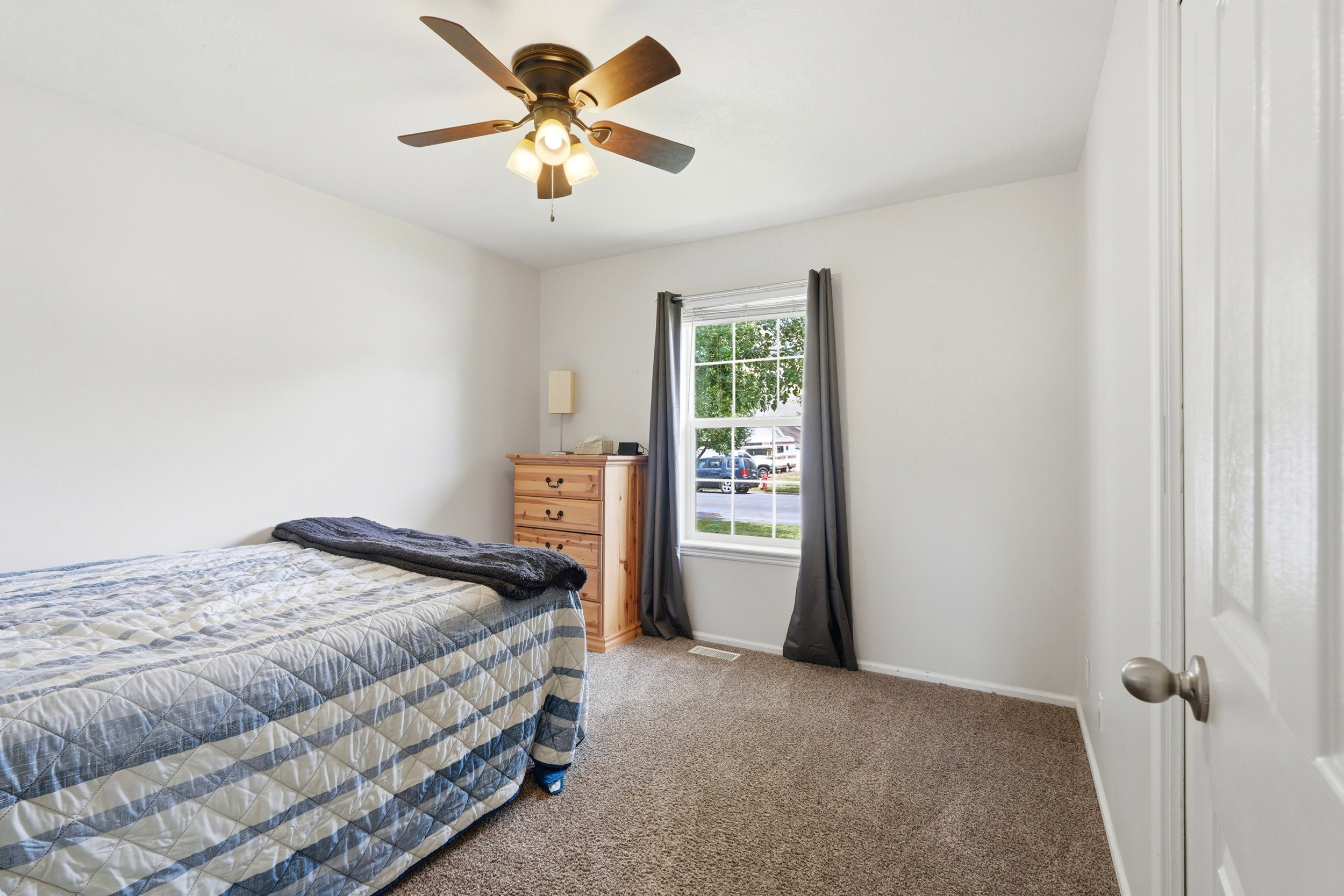 Carpeted room featuring a ceiling fan with integrated lighting, a window with curtains, and white walls