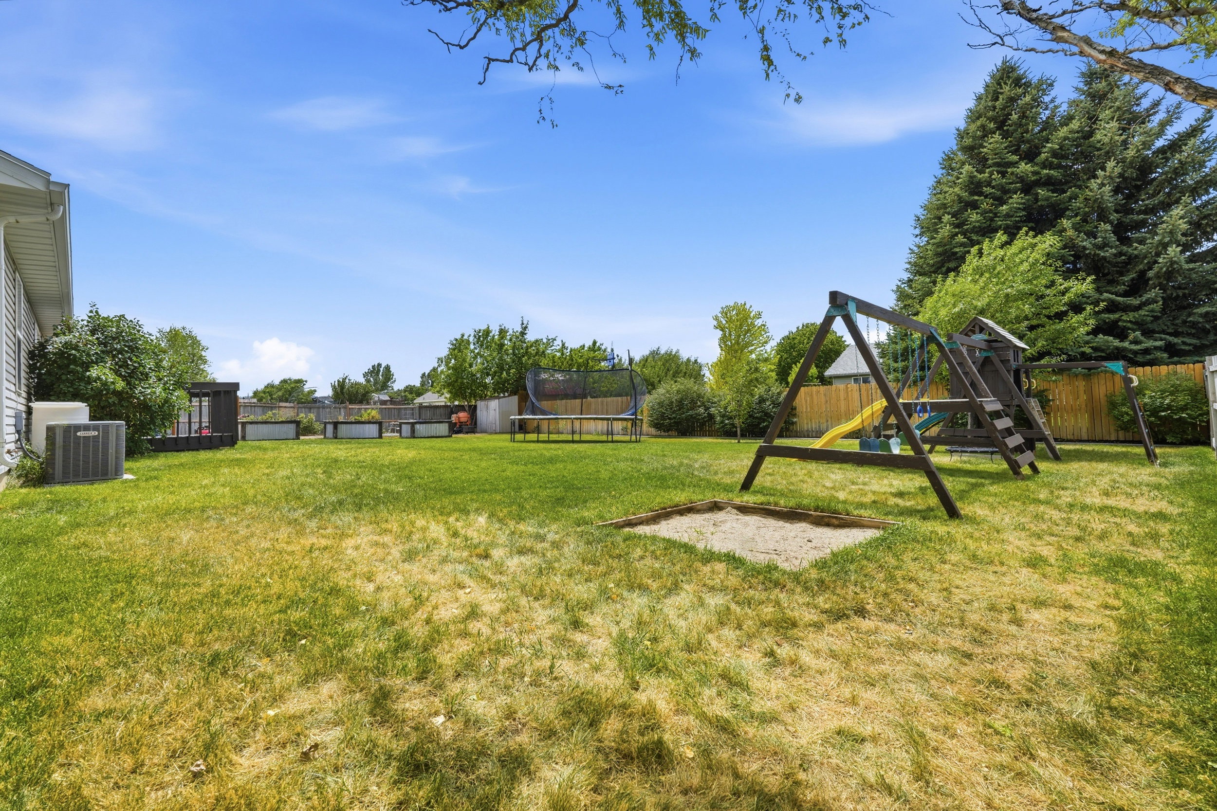Spacious backyard featuring a manicured lawn, sand pit, and mature trees