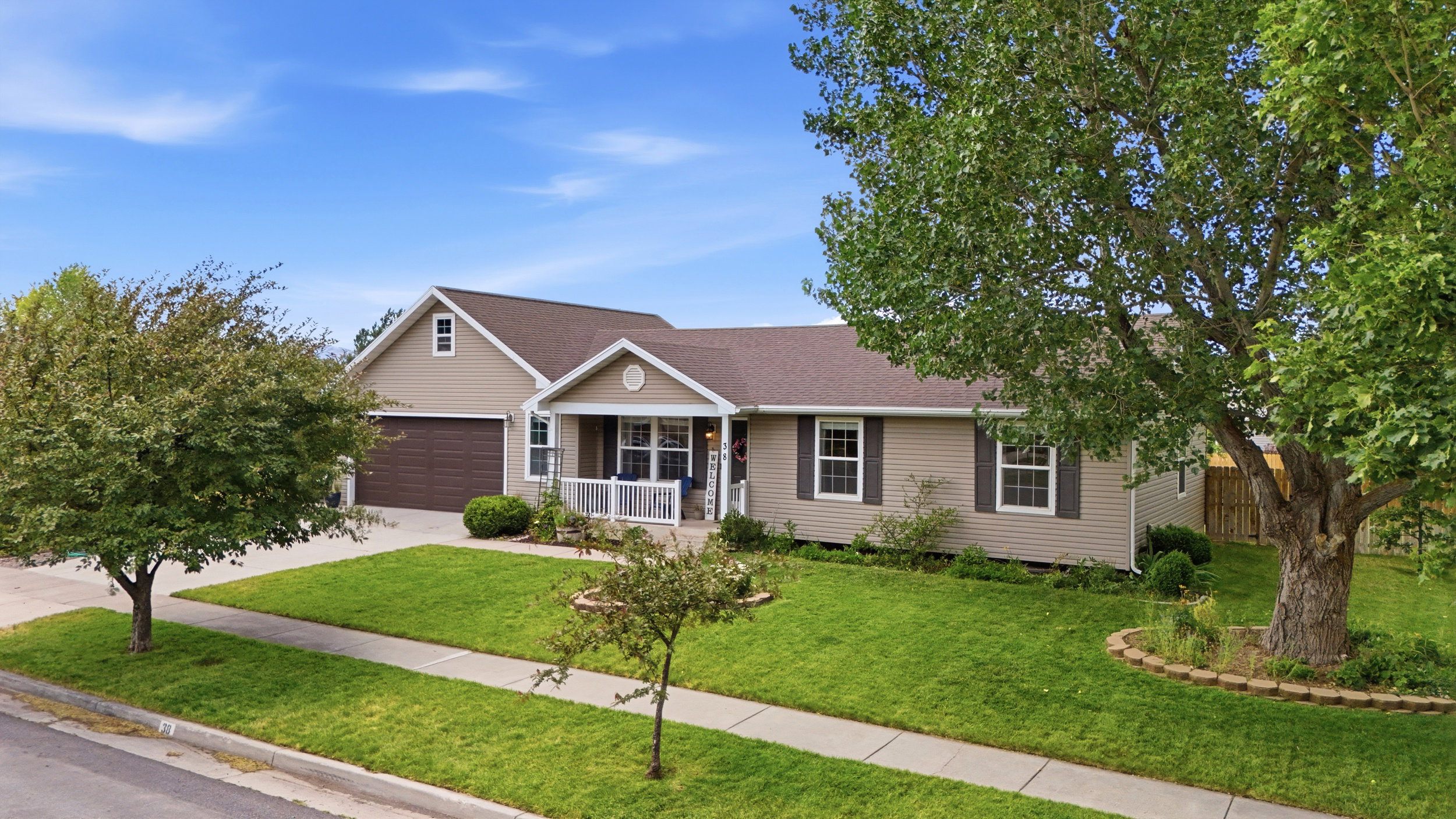 Single-story residence featuring light brown siding, a dark brown roof, and a covered front porch with white railings