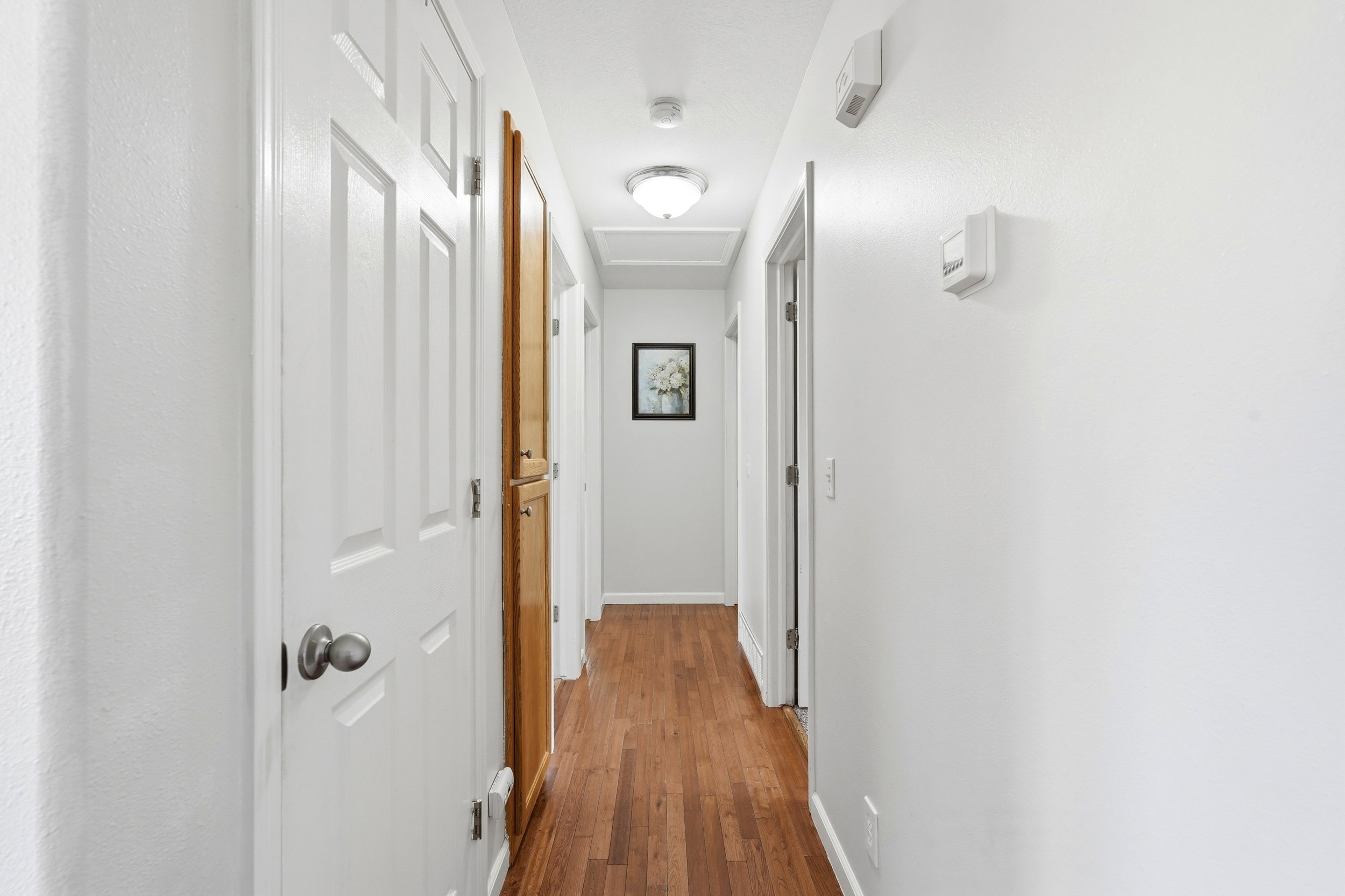 Hallway featuring wood-finish flooring, white walls, and white paneled doors with satin nickel hardware
