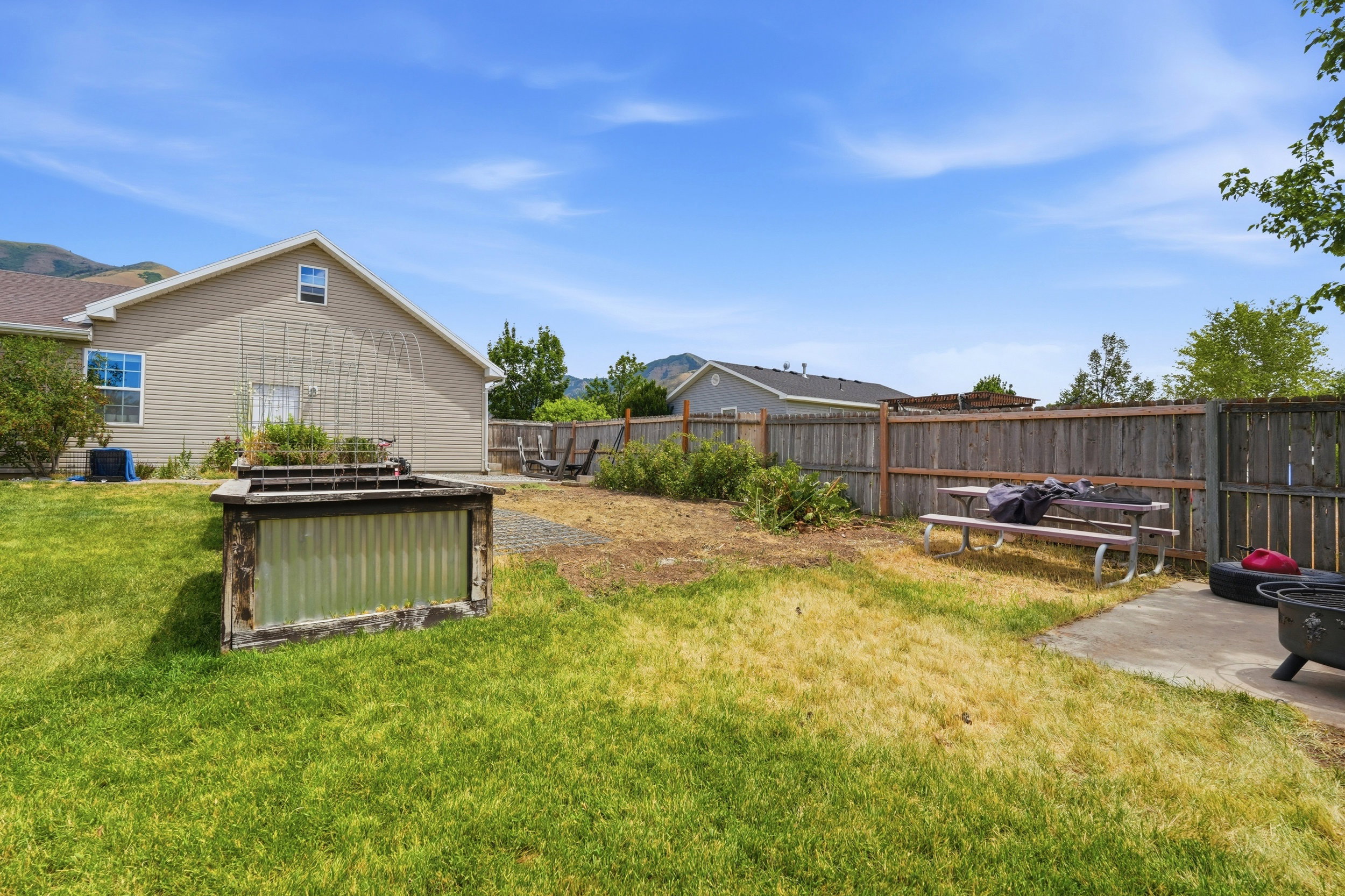 Expansive backyard featuring a raised garden bed, full privacy fencing, and a concrete patio area