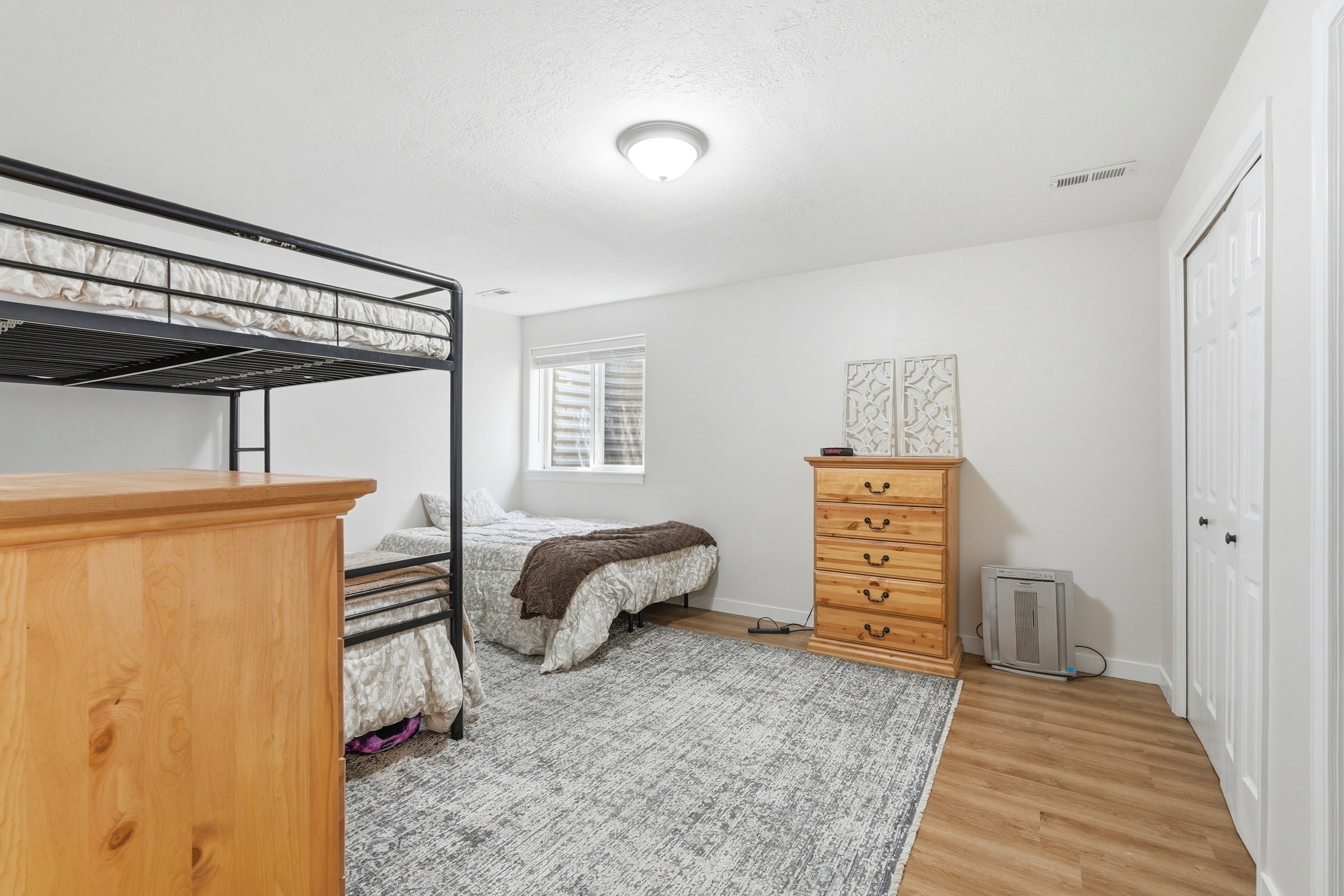 Spacious interior room featuring light wood-finish flooring, a neutral color palette, and a window with blinds