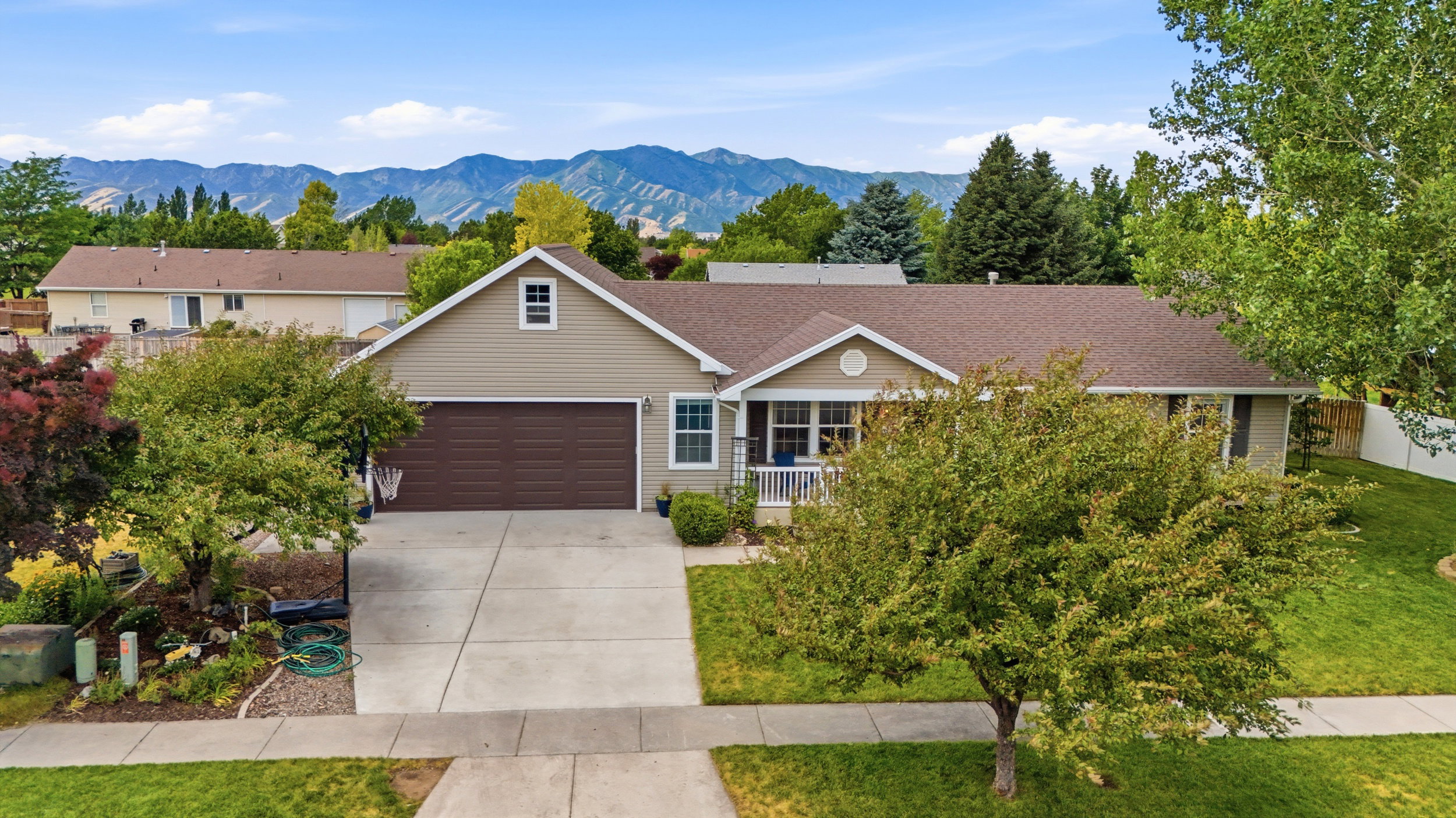 Ranch-style residence featuring a two-car garage, covered front porch, and mature landscaping