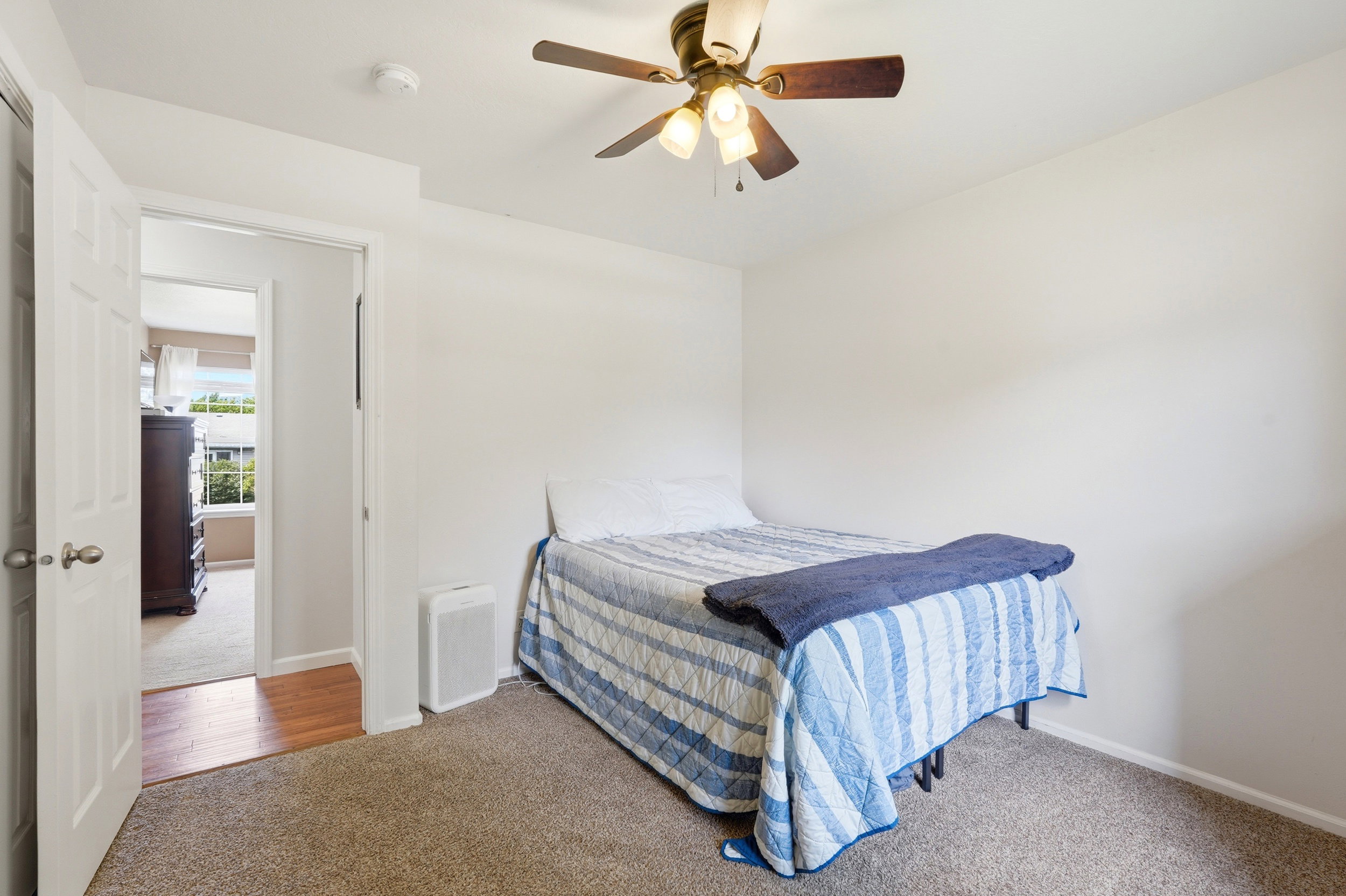 Carpeted room featuring a ceiling fan with integrated lighting, white walls, and a white door with a silver knob